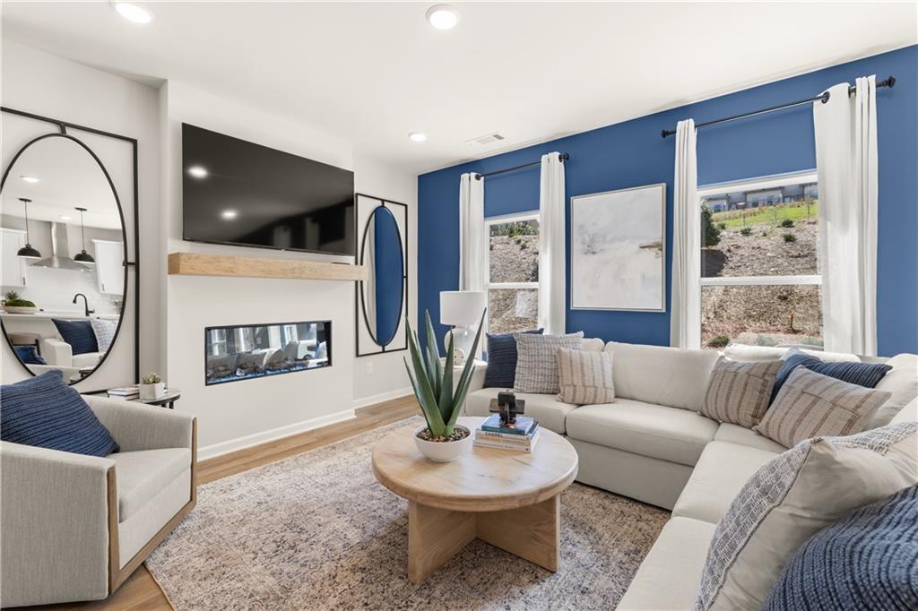 Cozy modern living room with white L-shaped sofa, linear gas fireplace, wall-mounted TV, blue accent wall, and large windows in Davidson Homes The Burton C, Canton, GA