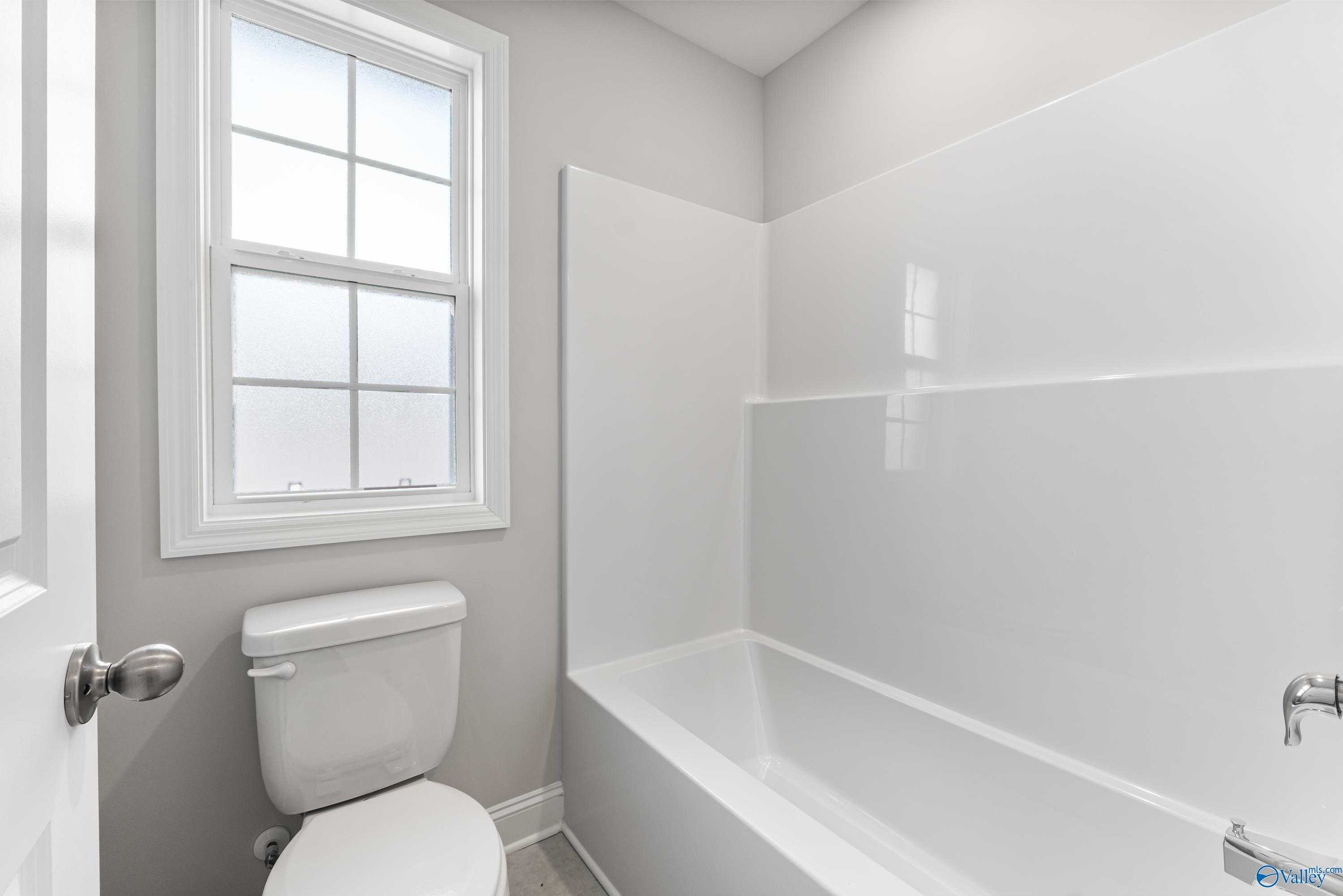 Modern white bathroom with bathtub, tiled shower enclosure, frosted window in Davidson Homes Madison A, Toney Alabama