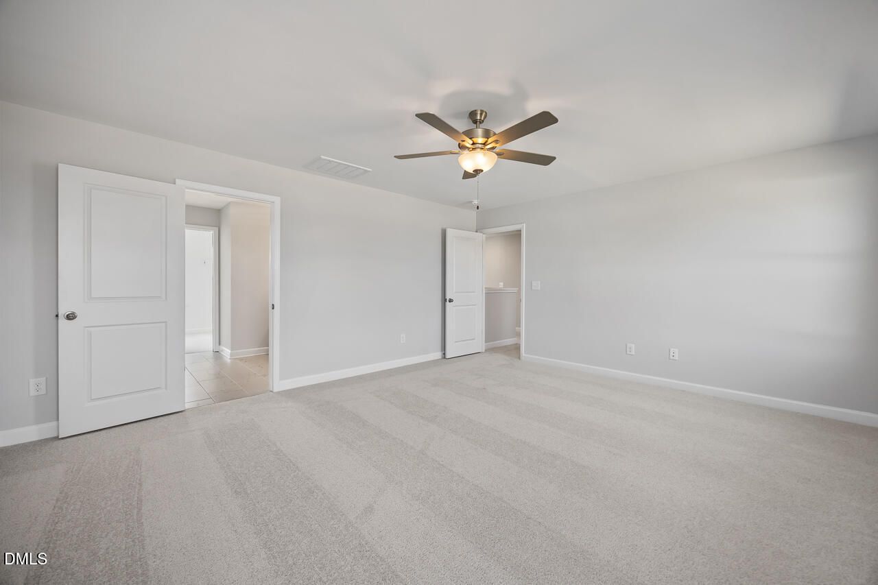 Spacious bedroom with light gray walls, beige carpet, ceiling fan, and open doors to attached bath in Davidson Homes The Willow G, Angier, NC