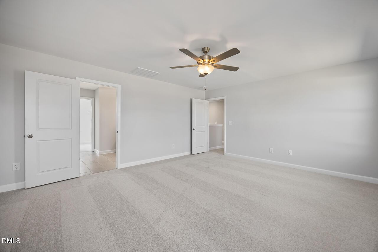 Spacious bedroom with light gray walls, beige carpet, ceiling fan, and open doors to attached bath in Davidson Homes The Willow G, Angier, NC