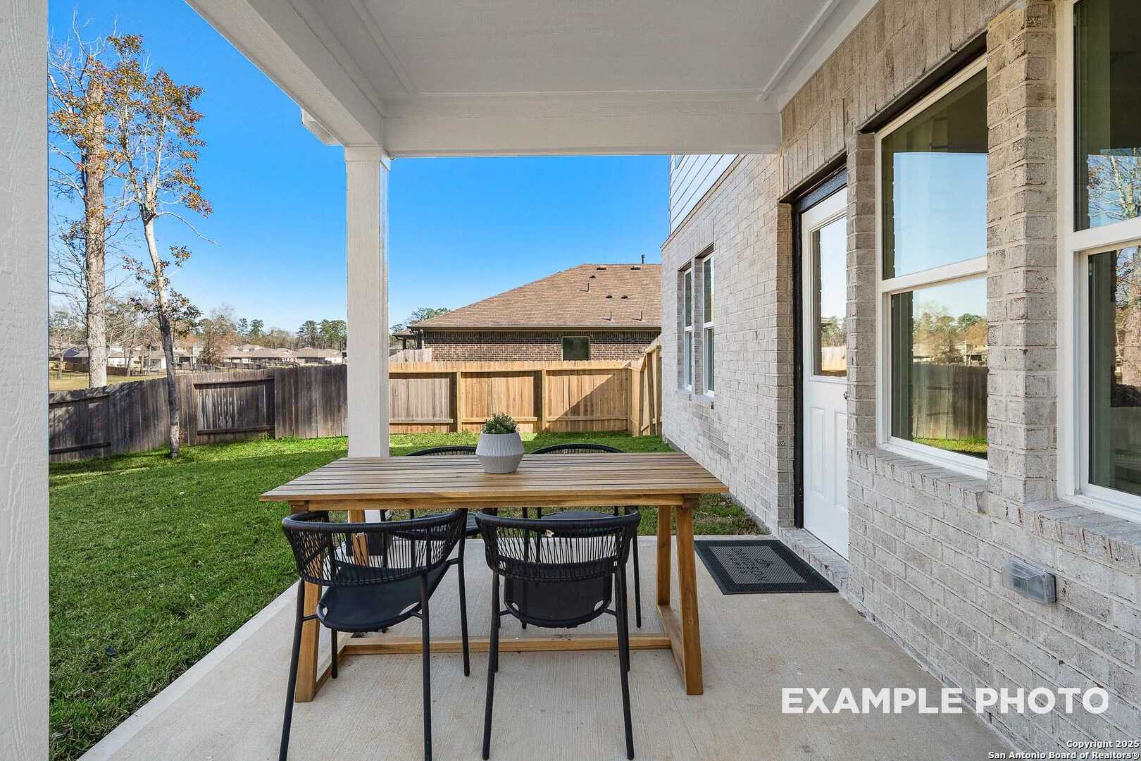 Covered back patio with teak table and rattan chairs overlooking fenced green backyard in Davidson Homes The San Marcos D, Agave, San Antonio