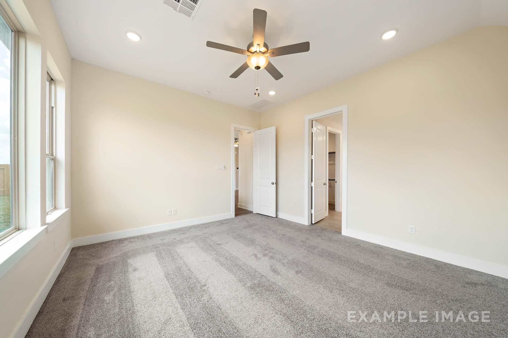 Spacious master bedroom in The Diana C featuring beige walls, gray carpet, ceiling fan, large windows, and walk-in closet door