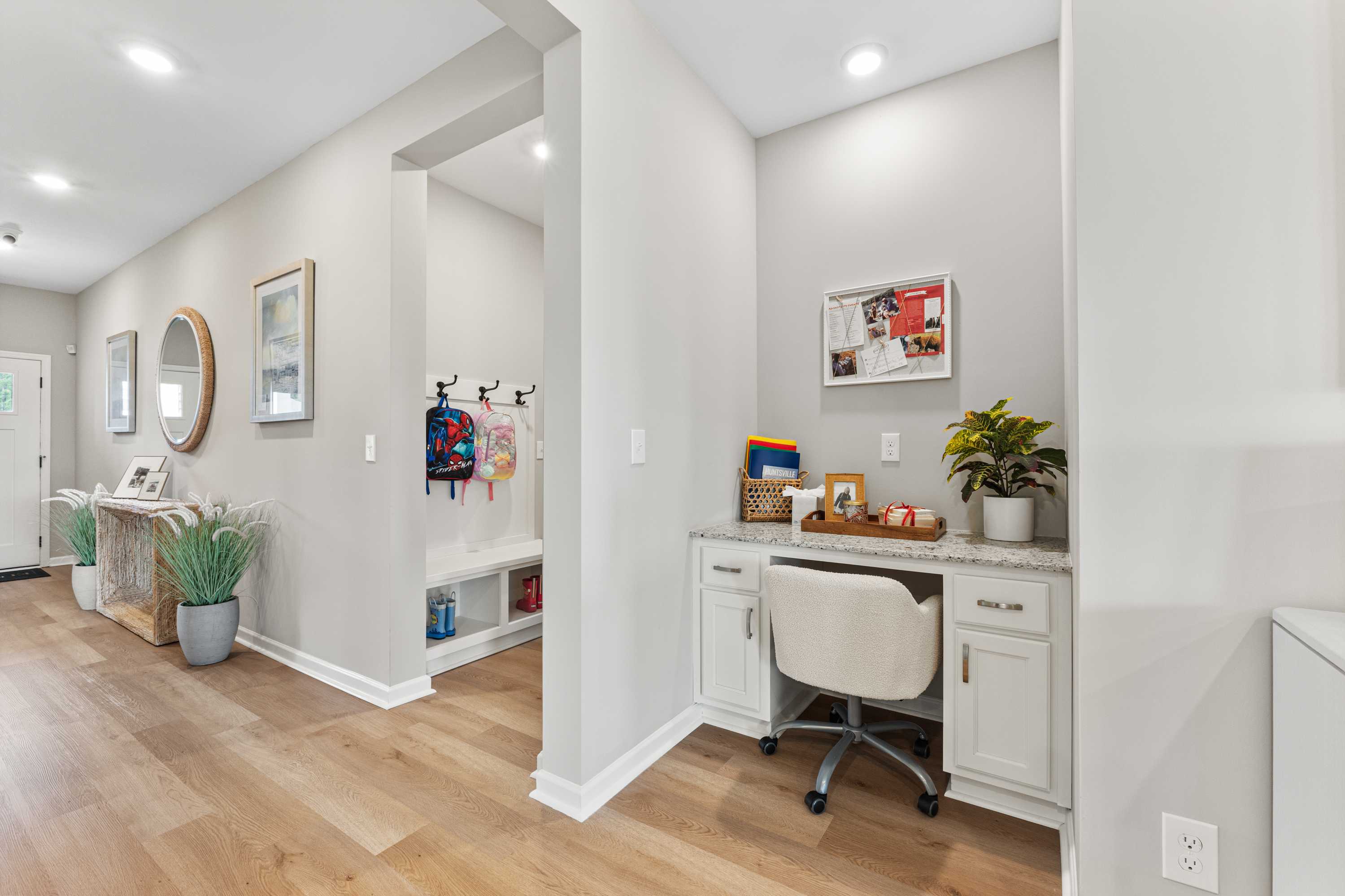 Spacious mudroom with built-in desk nook at Forest Glen in Hazel Green, Alabama featuring hardwood floors, white cabinetry, and coat hooks