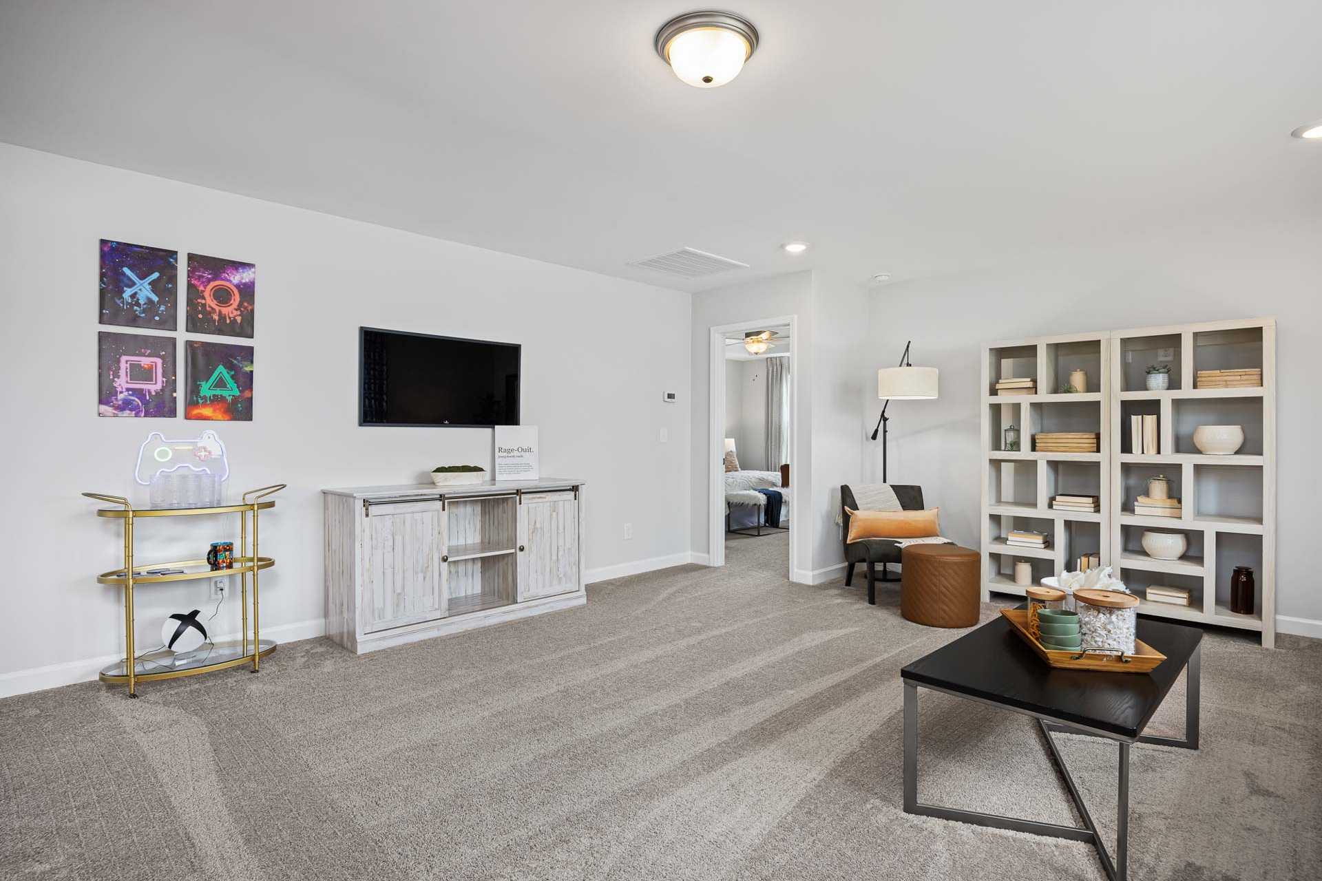 Spacious modern bonus room at Beverly Place in Four Oaks NC with white entertainment center, mounted TV, bookshelves and PlayStation art