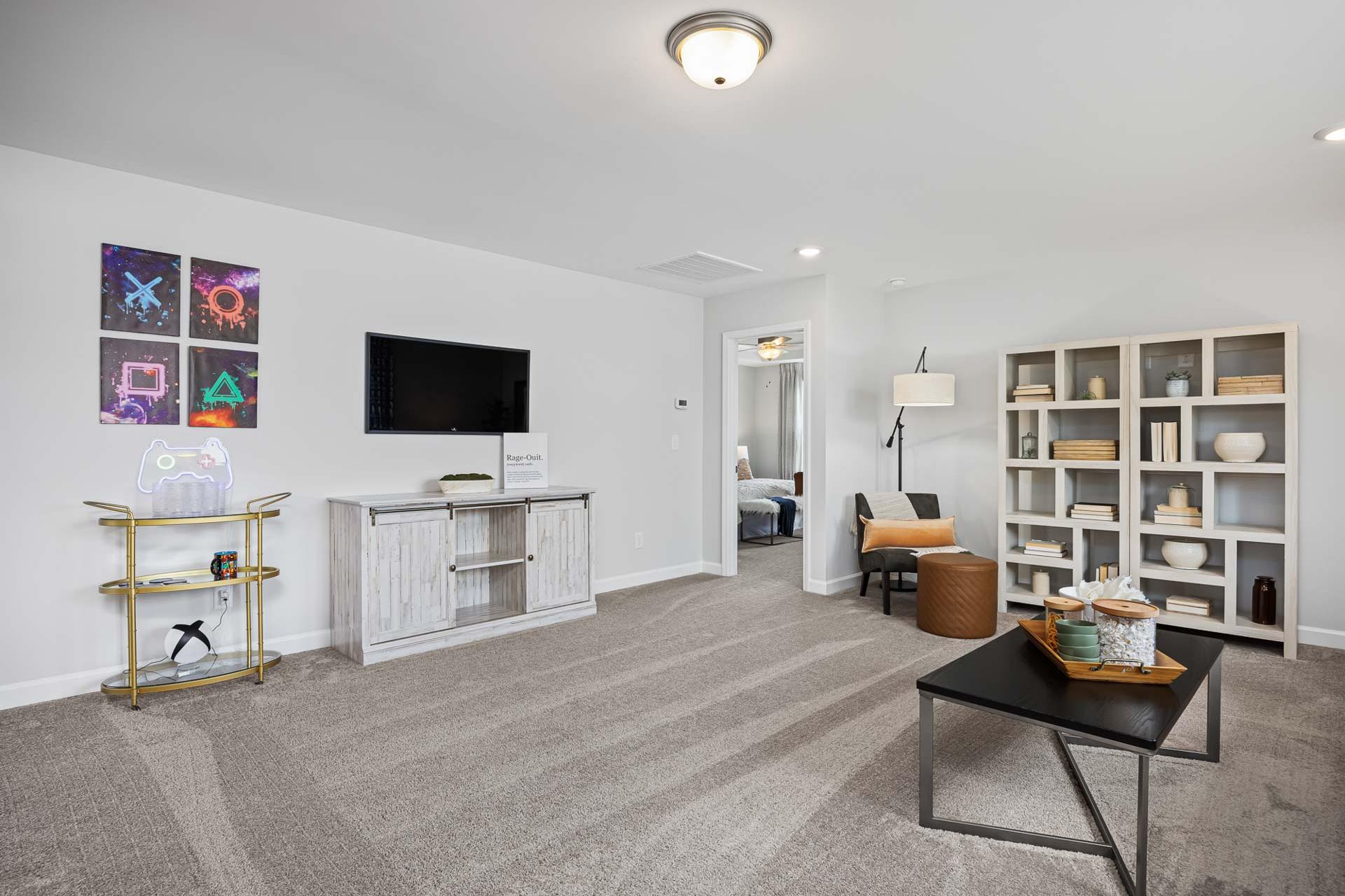 Spacious modern bonus room at Beverly Place in Four Oaks NC with white entertainment center, mounted TV, bookshelves and PlayStation art