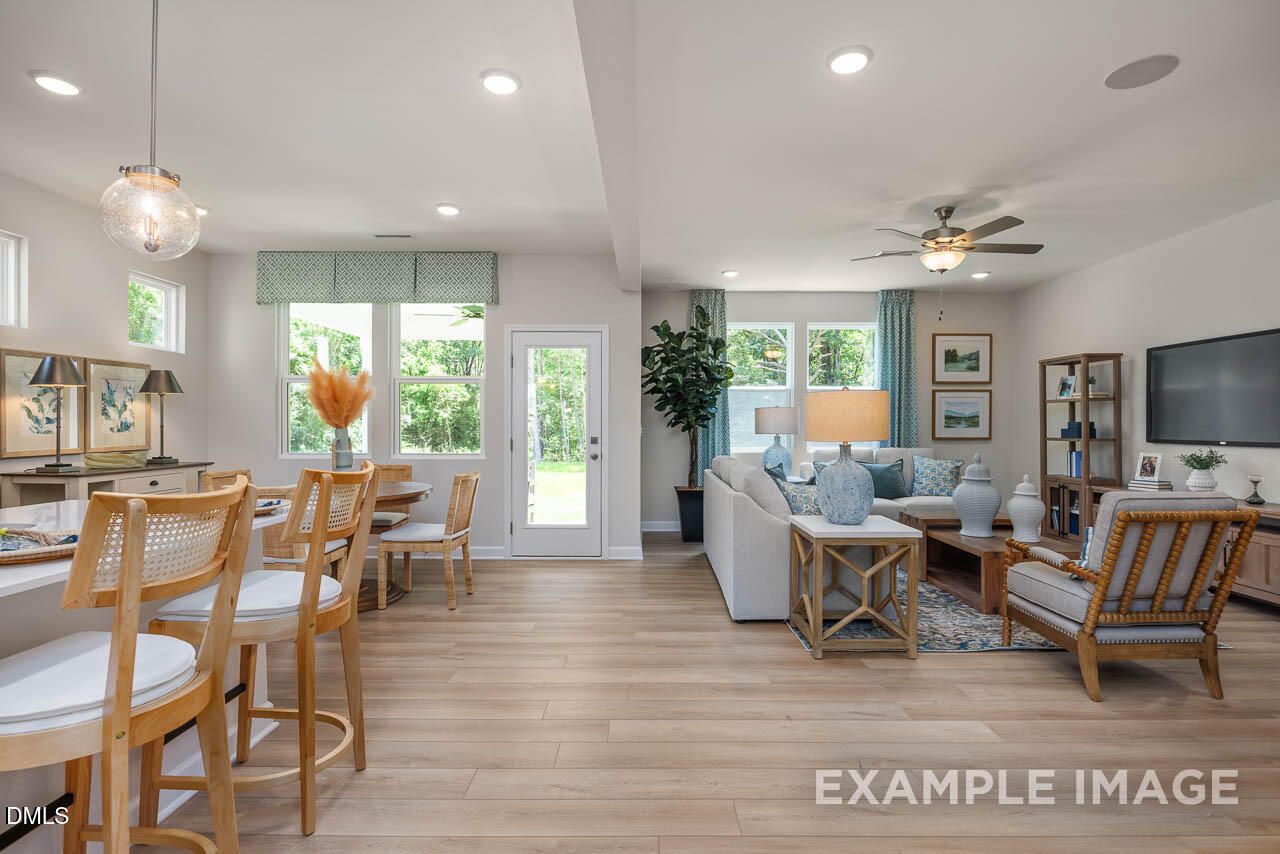 Bright open-concept living and dining room with modern sofa, wooden table, large windows, and sliding doors in Lillington 4-bedroom Willow B home