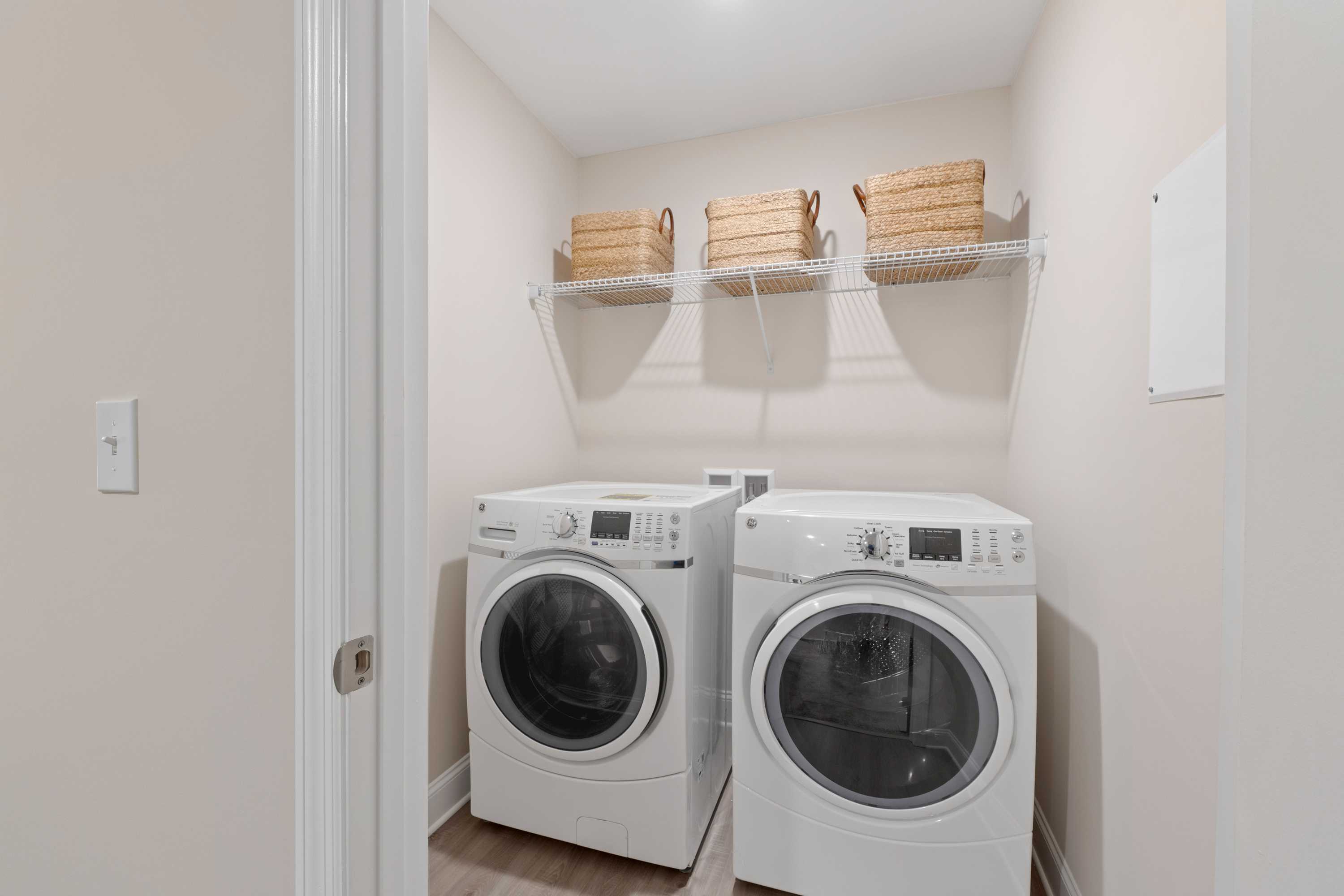 Spacious laundry room in Pavilion Huntsville AL with white front-load washers dryers and wicker basket shelves