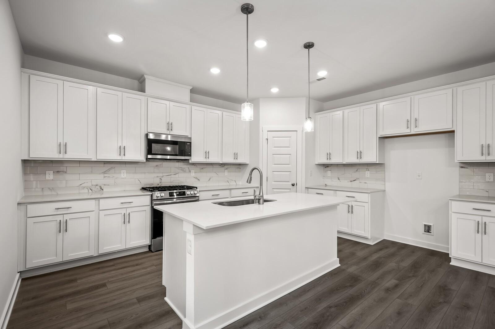 Modern kitchen with white cabinets, quartz countertops, and center island in The Logan C floor plan at Calista Farms.