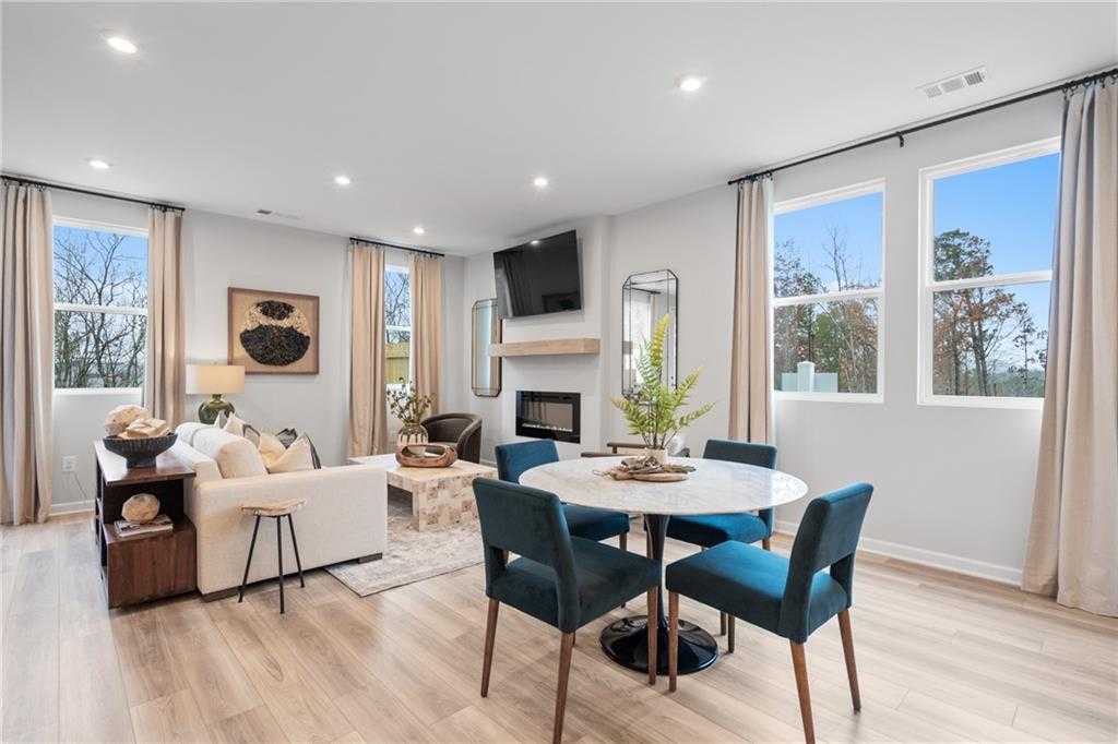 Cozy living room with fireplace, mounted TV, blue-upholstered dining chairs, and large windows in Davidson Homes The Wilmington B, Emerson, GA
