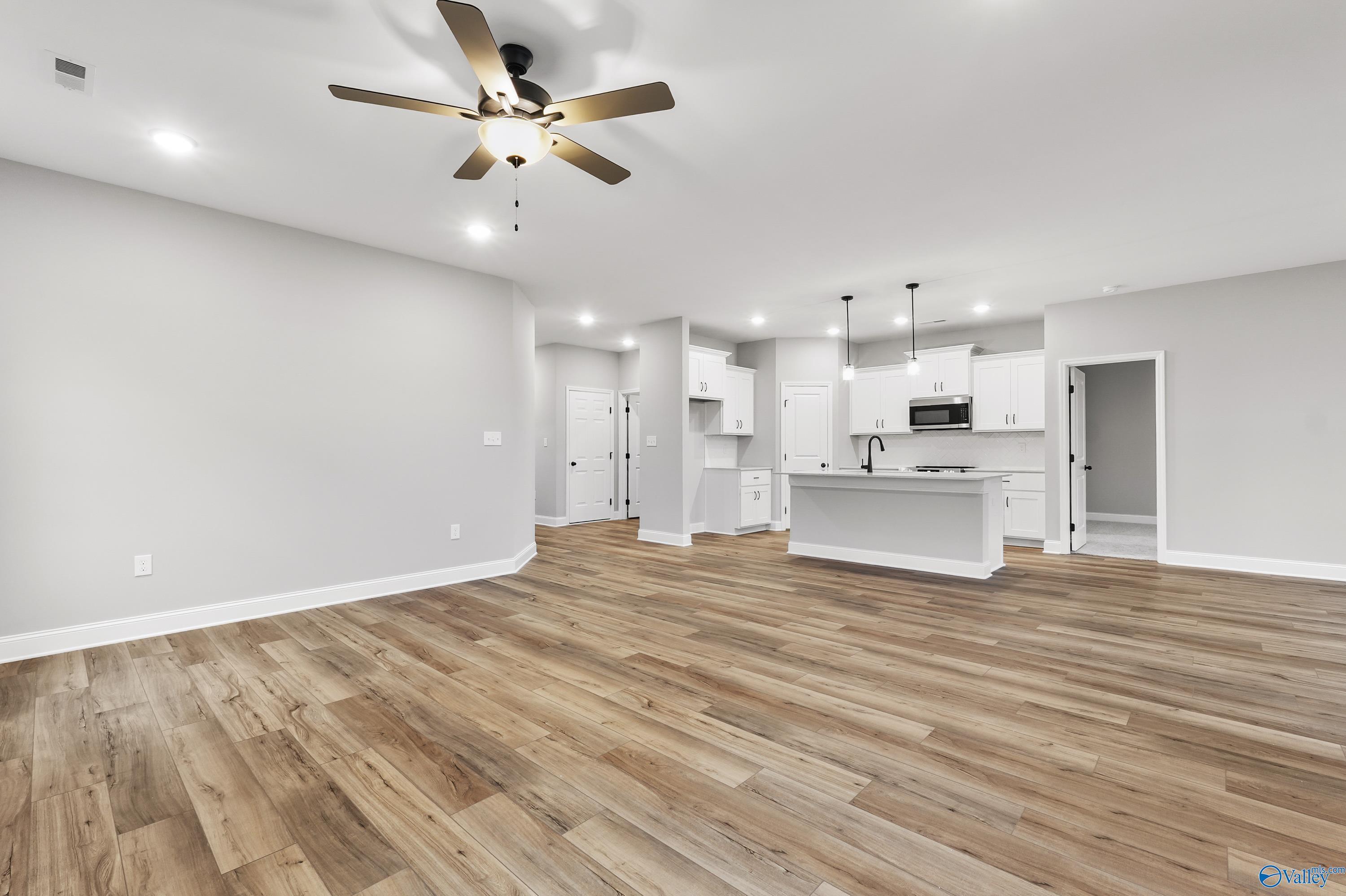 Open-concept kitchen with white cabinets, island sink, stainless appliances, and hardwood floors in The Asheville C, Meridianville, AL