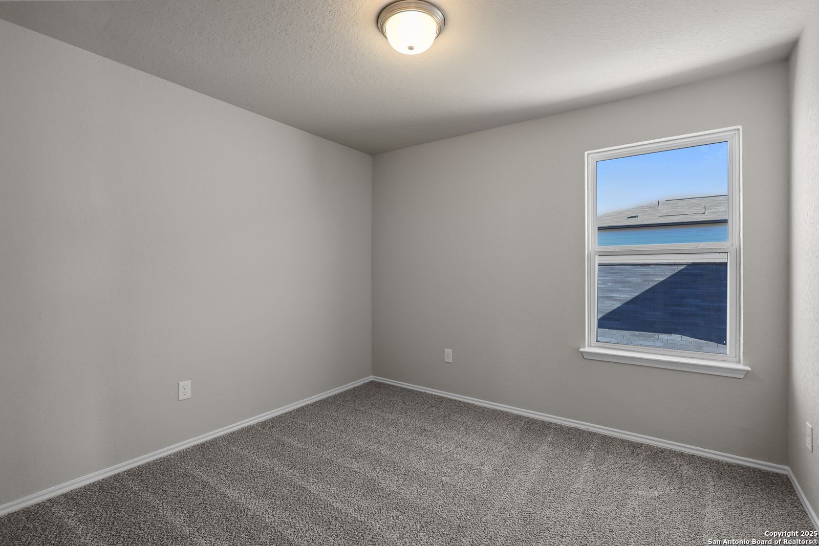 Bright secondary bedroom with light gray walls, plush gray carpet, and large window overlooking blue sky in Davidson Homes The Trinity D, San Antonio