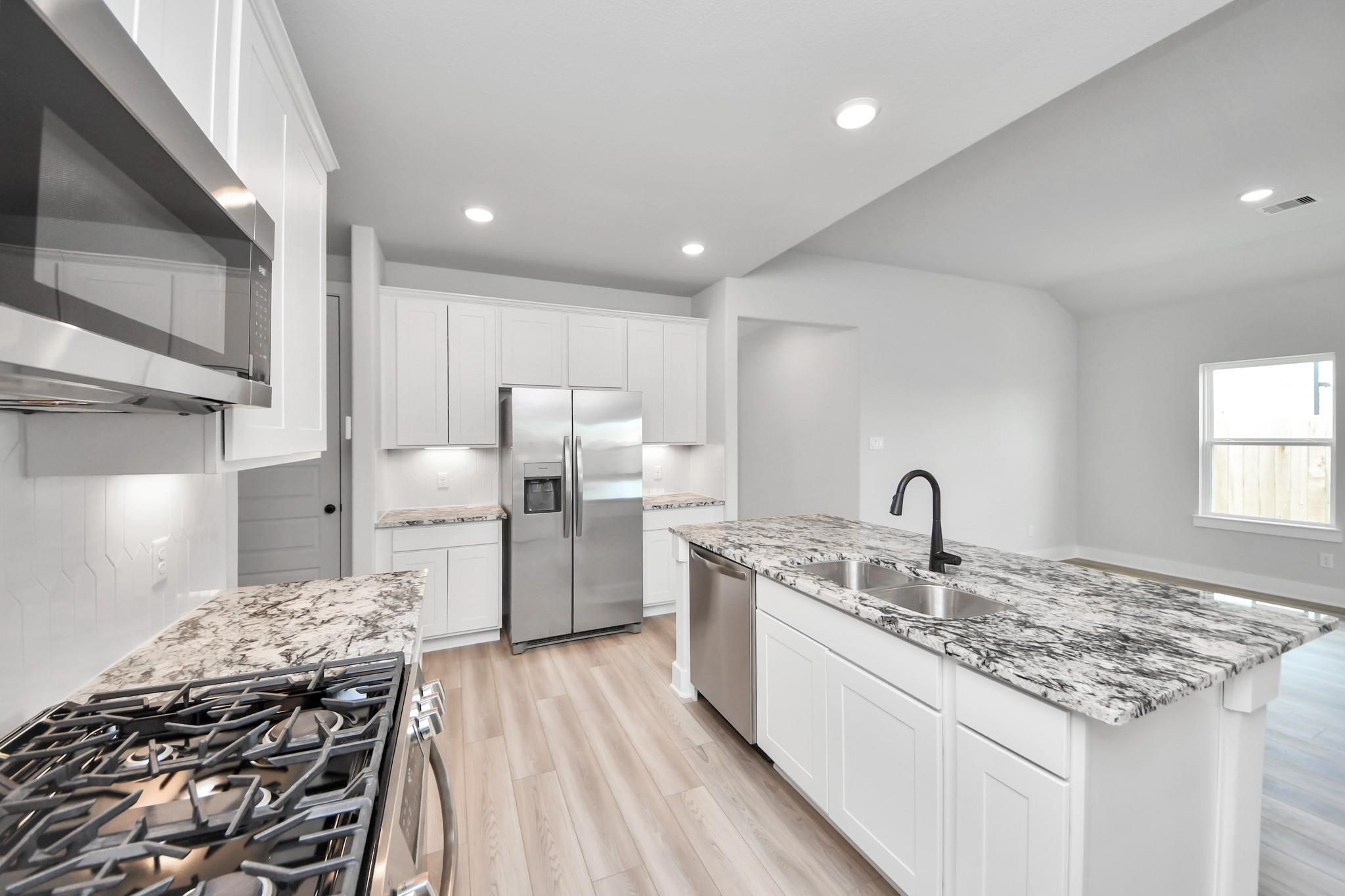 Modern kitchen with granite island, stainless appliances, and white cabinets in The Laguna C floor plan at Sunterra, Katy.