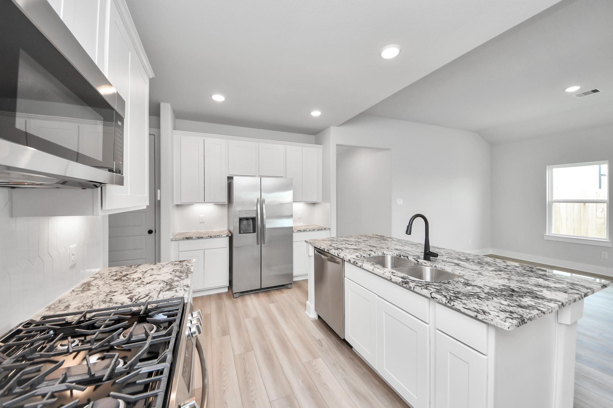 Modern kitchen with granite island, stainless appliances, and white cabinets in The Laguna C floor plan at Sunterra, Katy.