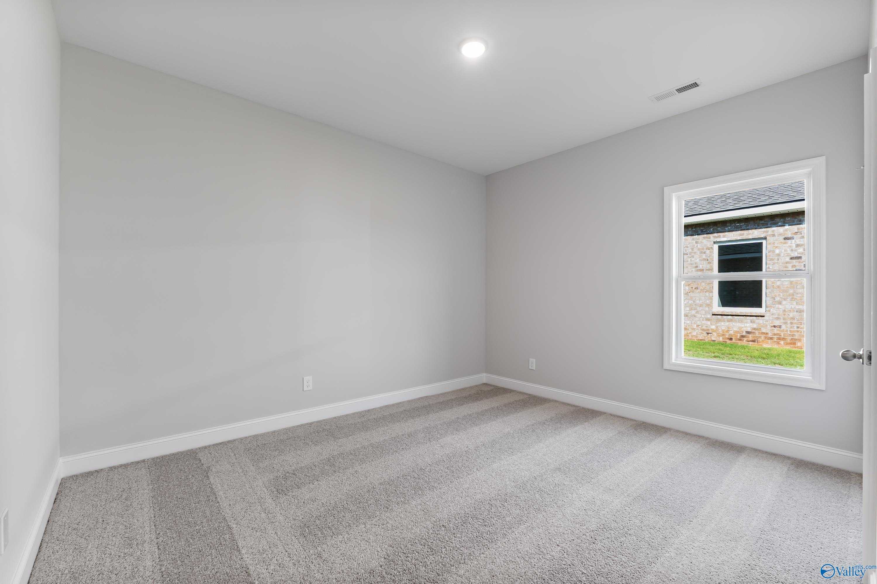 Neutral gray bedroom with plush carpet, large window view, and recessed lighting in Davidson Homes The Daphne, Hazel Green, Alabama