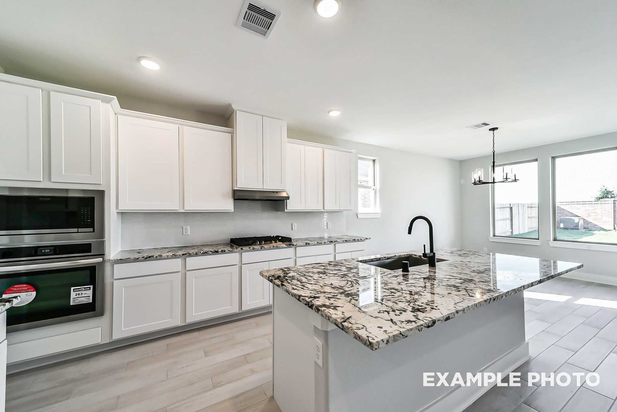 Modern kitchen featuring white shaker cabinets, speckled granite island with sink, stainless oven in The Philip C by Davidson Homes, Rosharon, TX