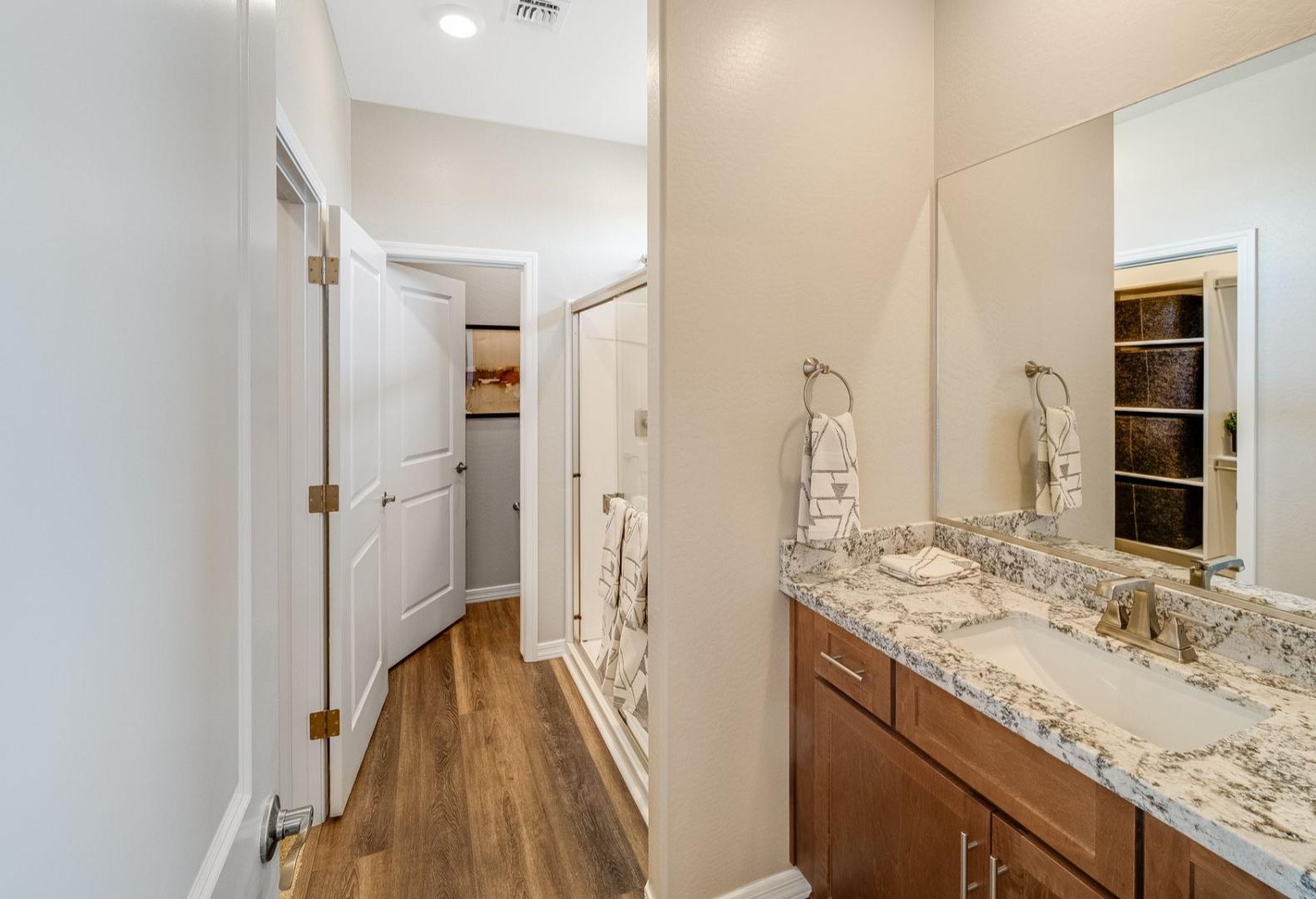 Master bathroom in The Savannah home design with quartz vanity, large mirror, walk-in shower, and wood flooring