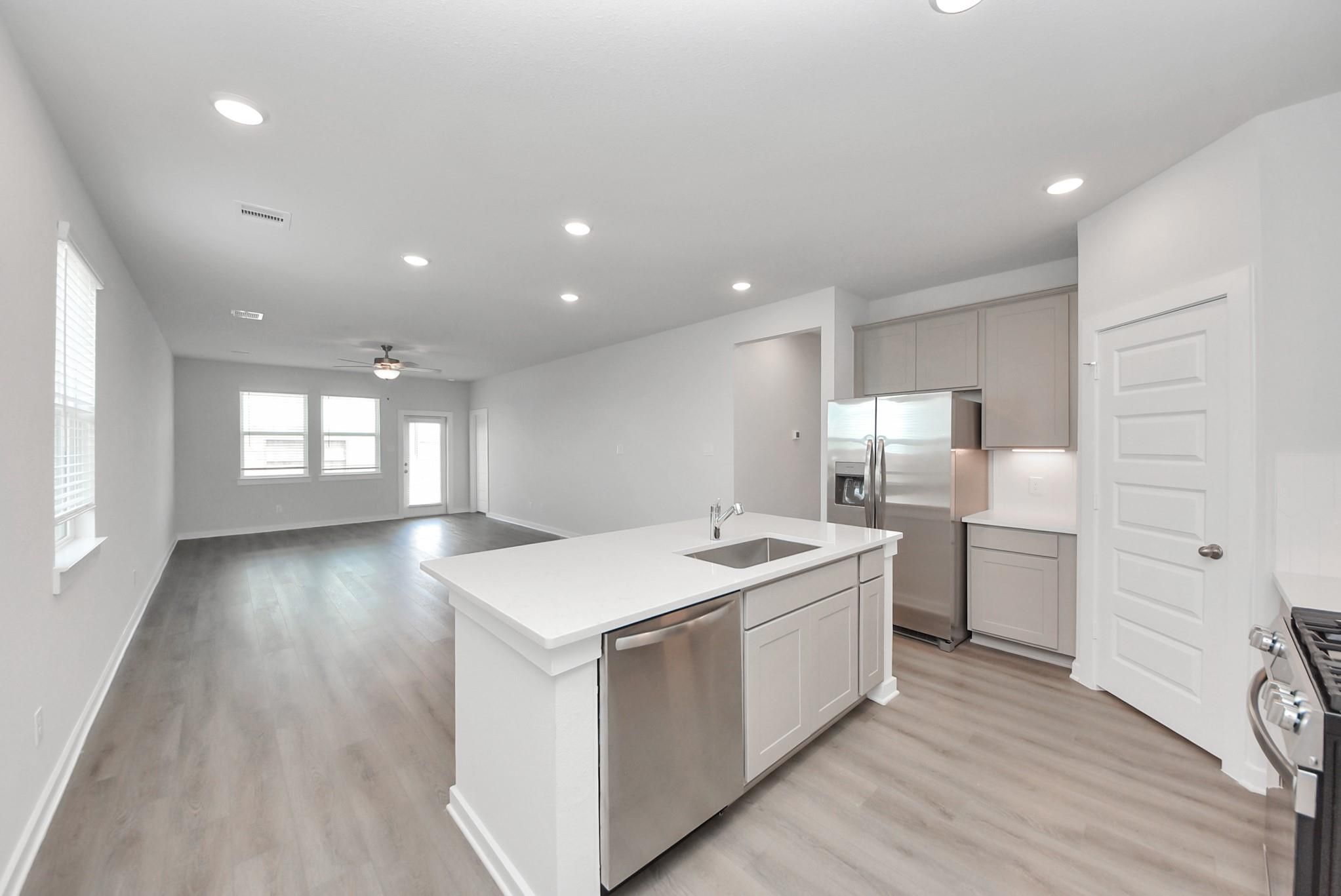 Bright open-concept kitchen with white island, sink, stainless appliances, and luxury vinyl plank flooring in Davidson Homes San Marcos E plan