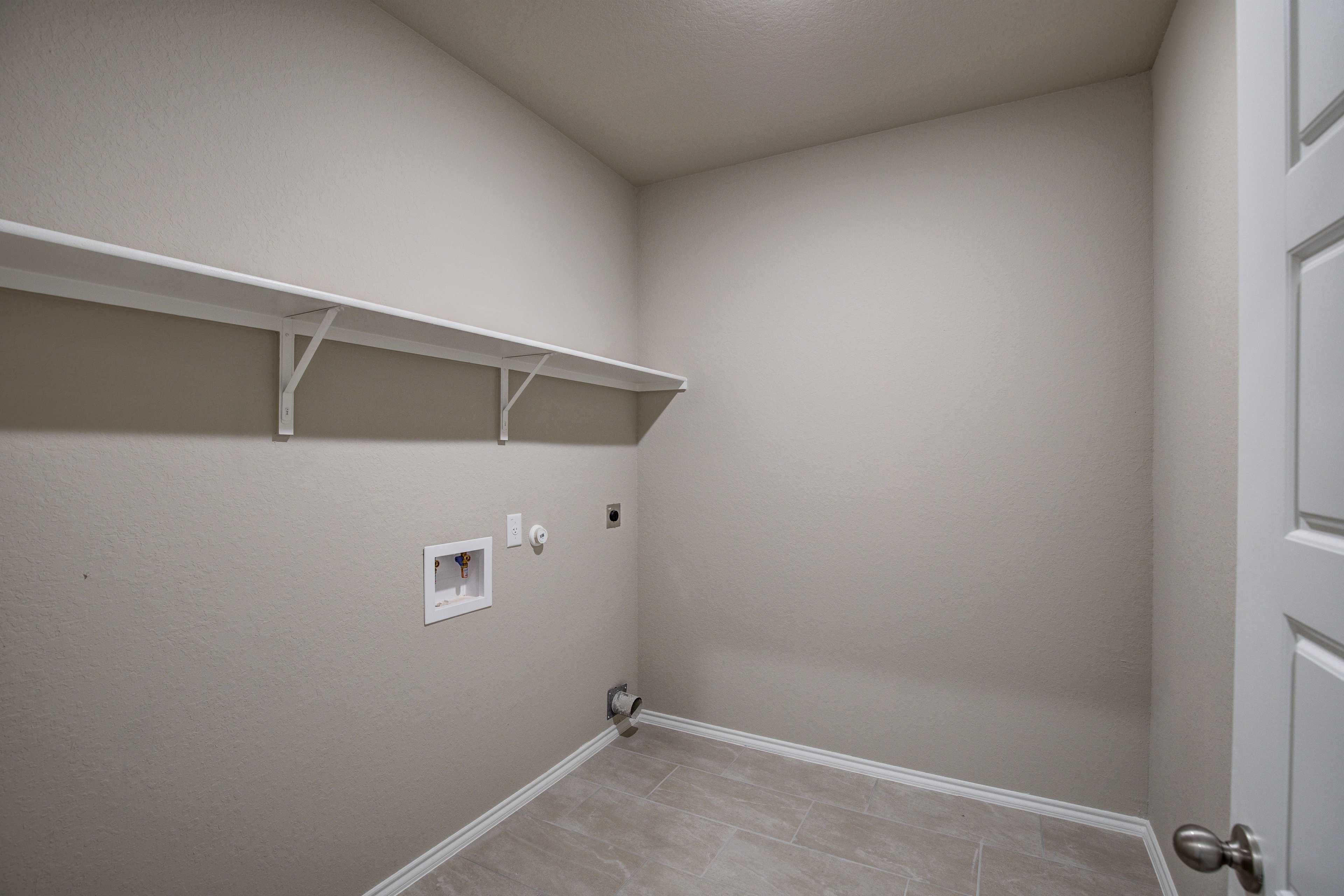 Spacious laundry room in The Murray Davidson Homes design with white wall shelves, washer-dryer hookups, and beige walls