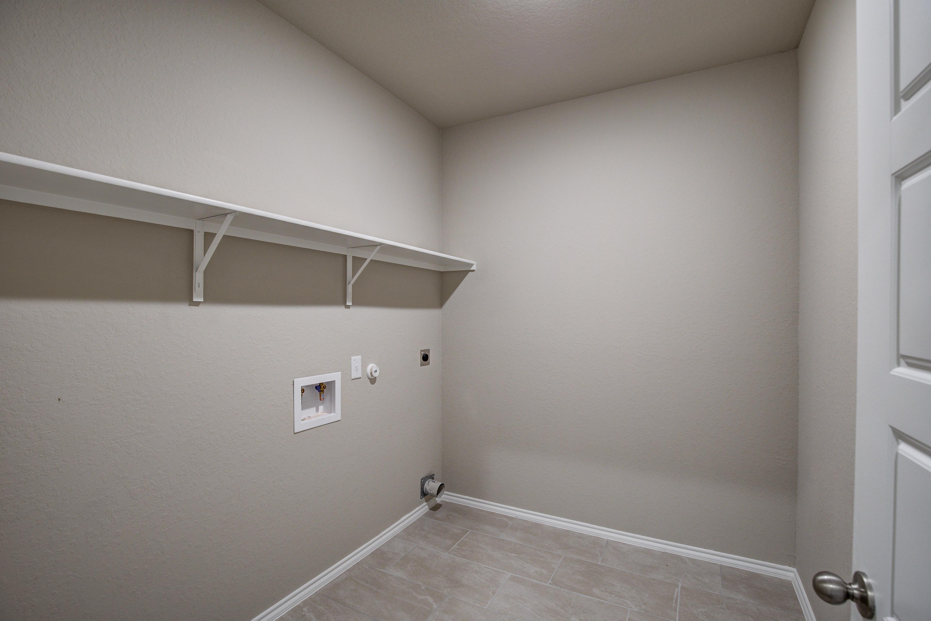 Spacious laundry room in The Murray G home with beige walls, white built-in shelves, washer dryer hookups, and tile floor