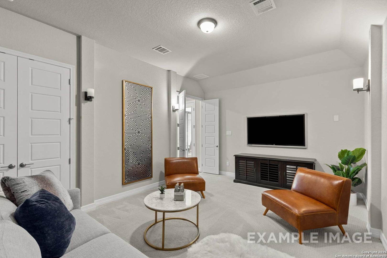Cozy media room with gray sofa, leather armchairs, mounted TV, and modern wall art in Davidson Homes The Summerlin B, Castroville, Texas