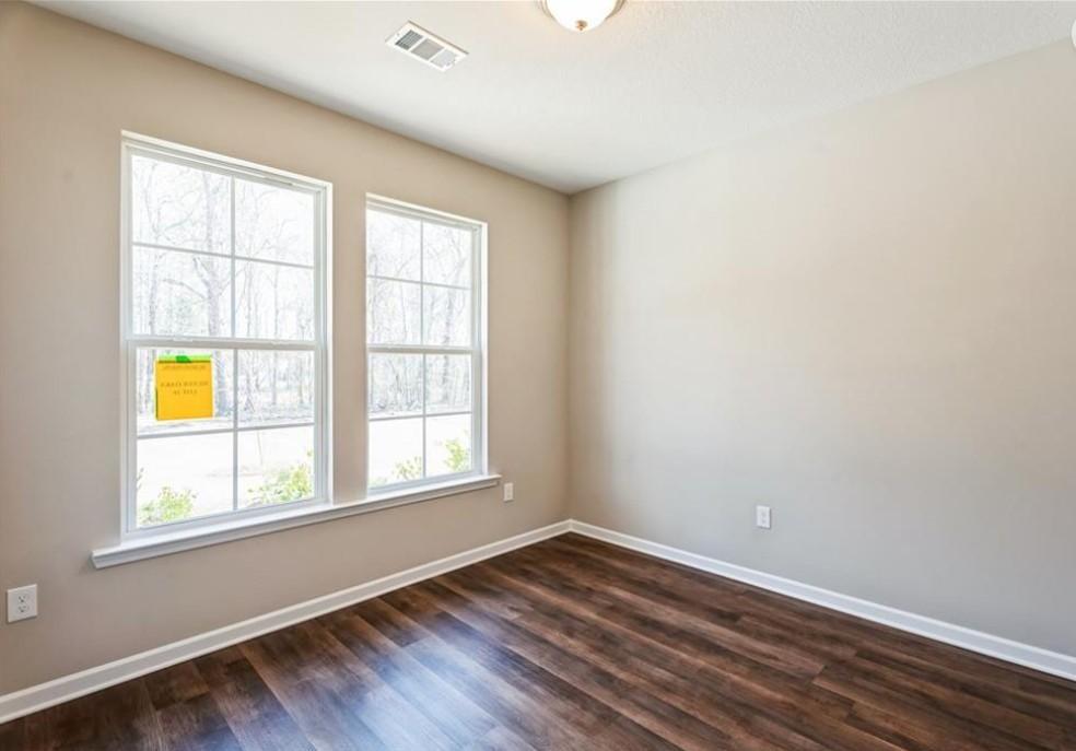 Bright secondary bedroom with double windows, beige walls, and hardwood floors in Evermore Homes The Aurora A, Cusseta, Alabama