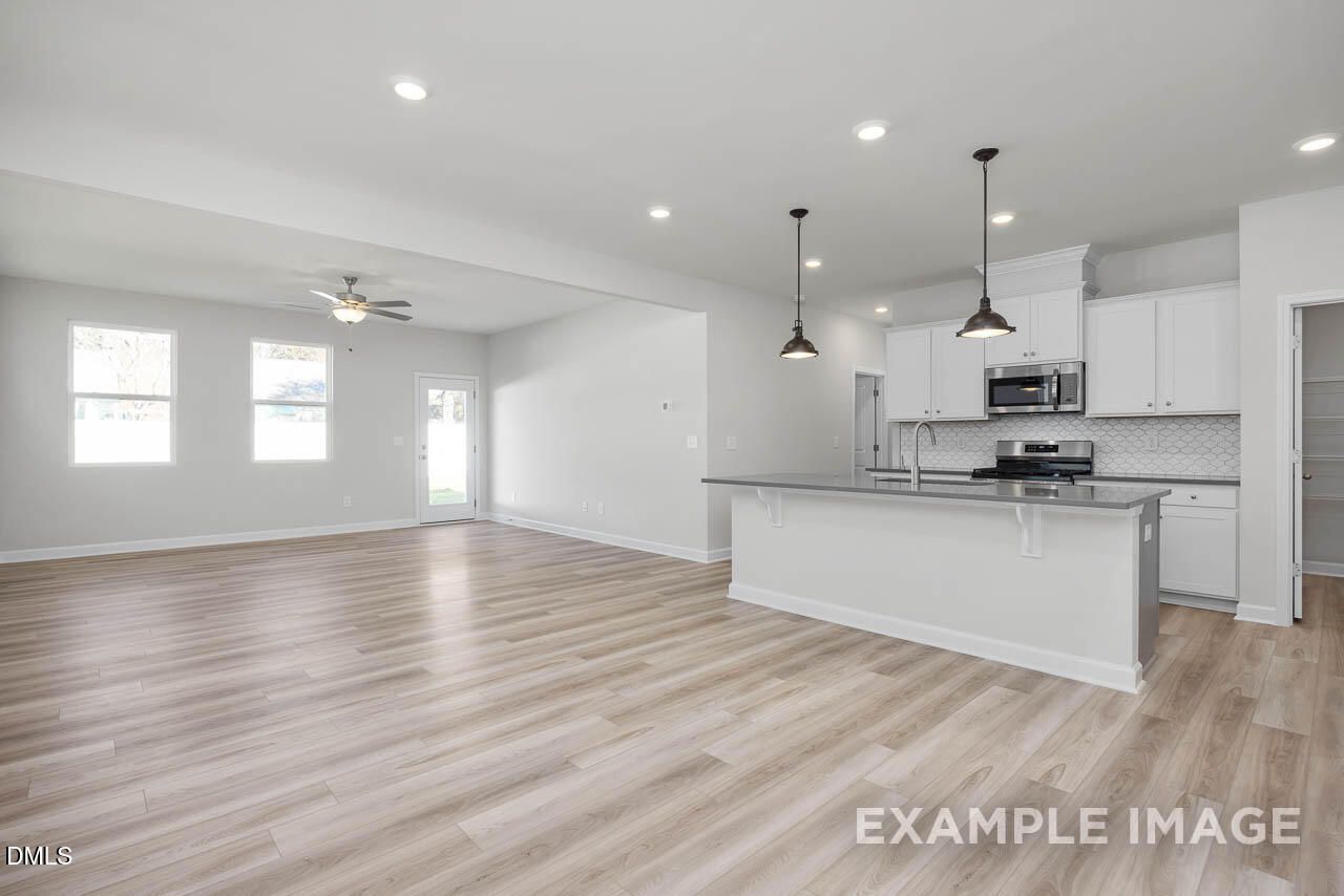 Open-concept kitchen with white cabinets, granite island, stainless appliances, and light wood floors in 4-bedroom Adalynn A home, Lillington, NC