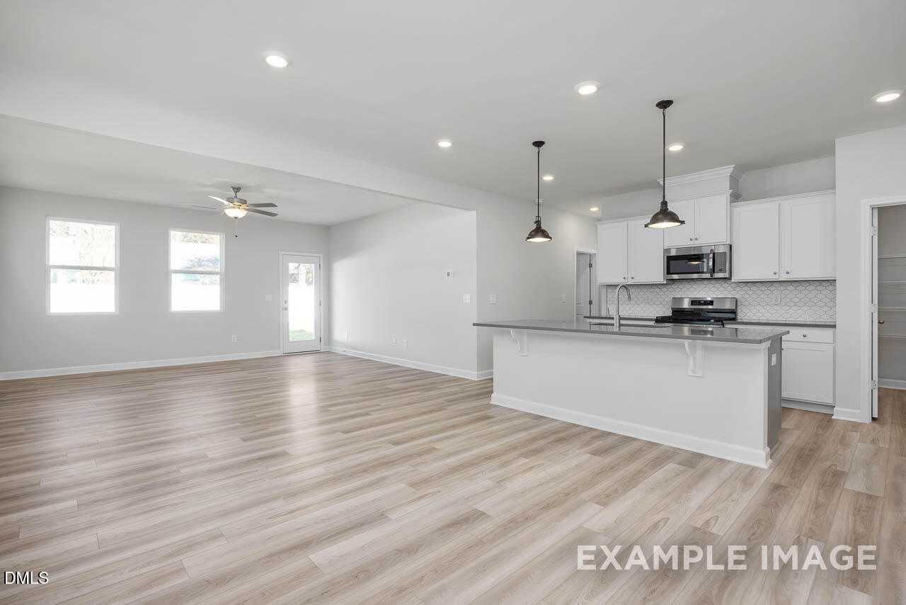 Open-concept kitchen with white cabinets, granite island, stainless appliances, and light wood floors in 4-bedroom Adalynn A home, Lillington, NC