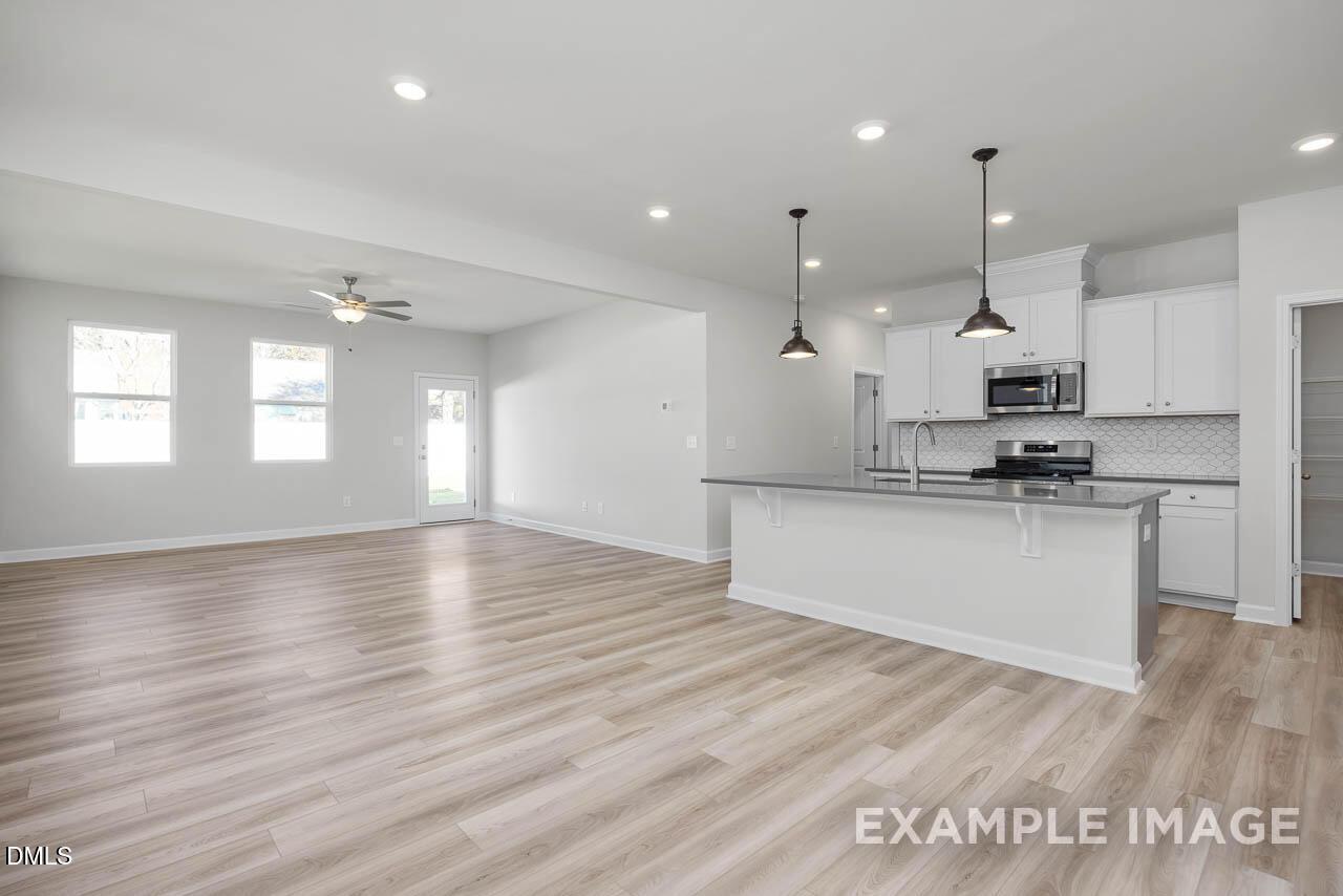 Spacious open-concept kitchen and living area with white island, stainless appliances, hardwood floors in The Adalynn A, Lillington, NC