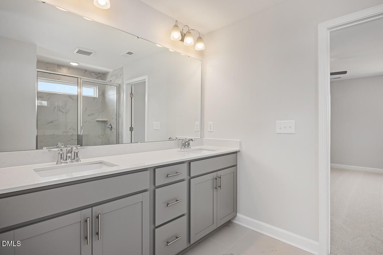 Modern master bathroom double vanity with quartz countertop, gray cabinets, large mirror, and glass shower in Davidson Homes The Willow G, Angier, NC