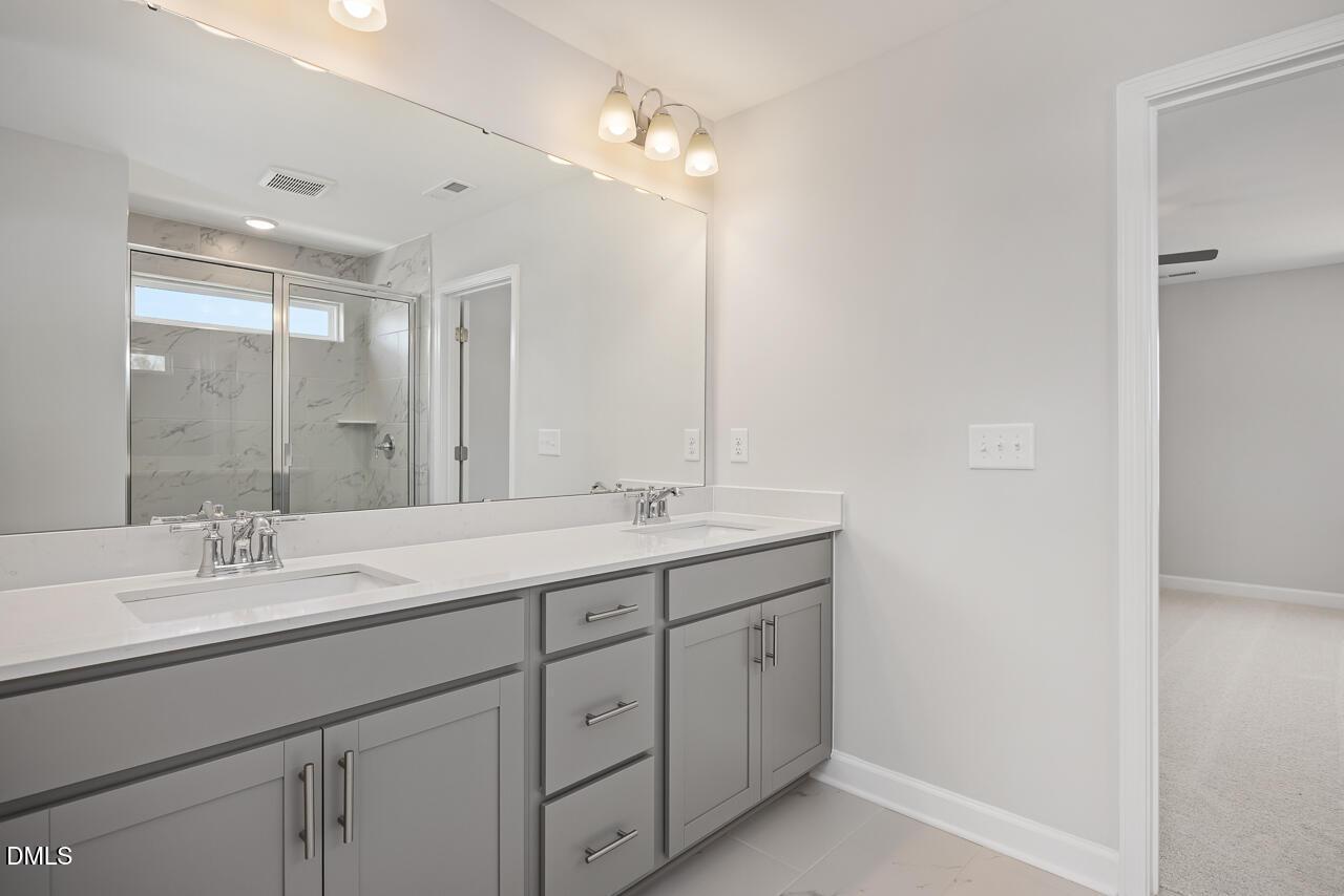 Modern master bathroom double vanity with quartz countertop, gray cabinets, large mirror, and glass shower in Davidson Homes The Willow G, Angier, NC