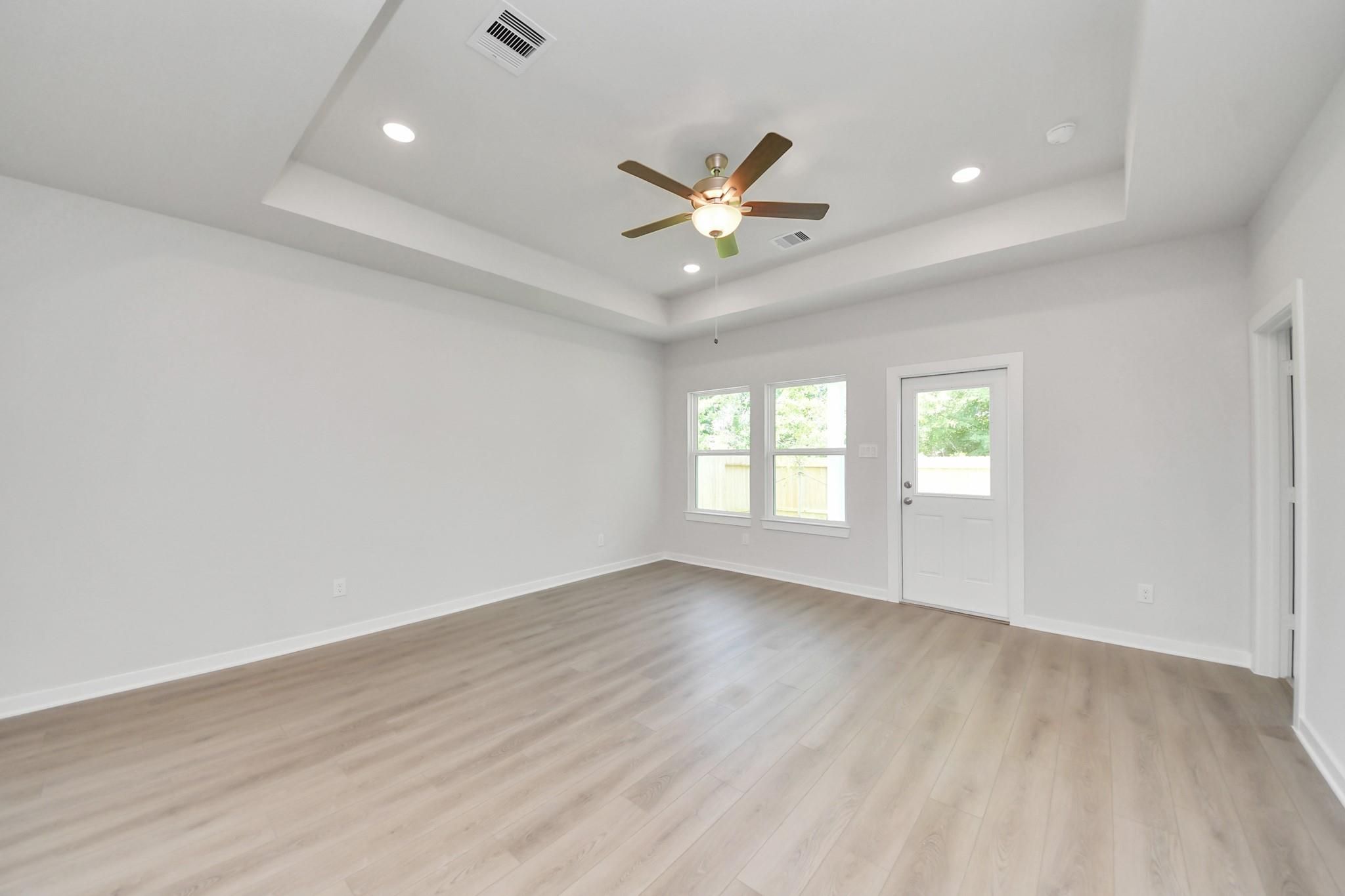 Spacious living area with tray ceiling and wood-look flooring in The Blanco E floor plan at Caney Creek Place, Conroe, TX.