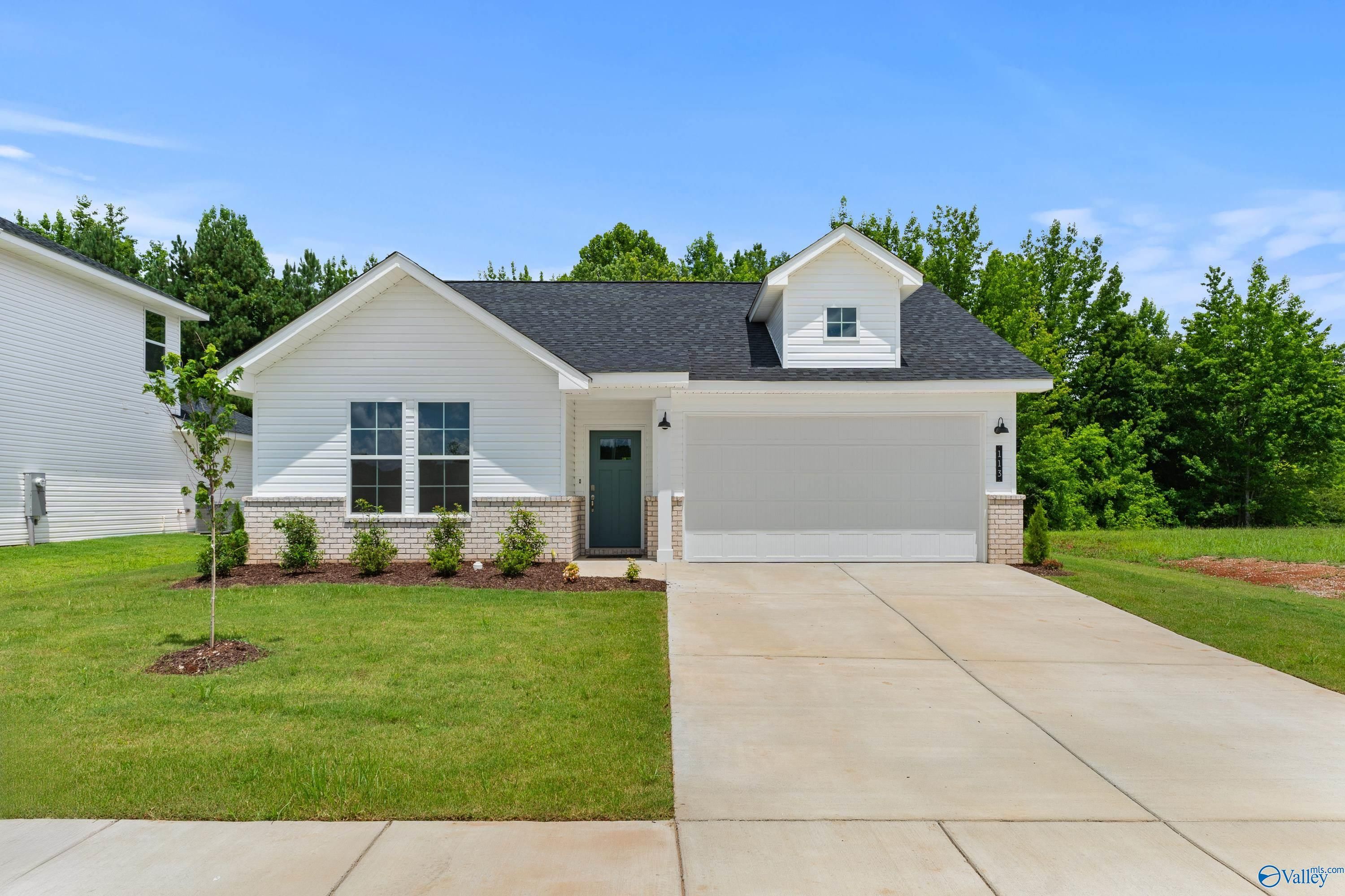 White single-story home with black roof, 2-car garage, landscaped yard and trees in Forest Glen, Hazel Green, Alabama