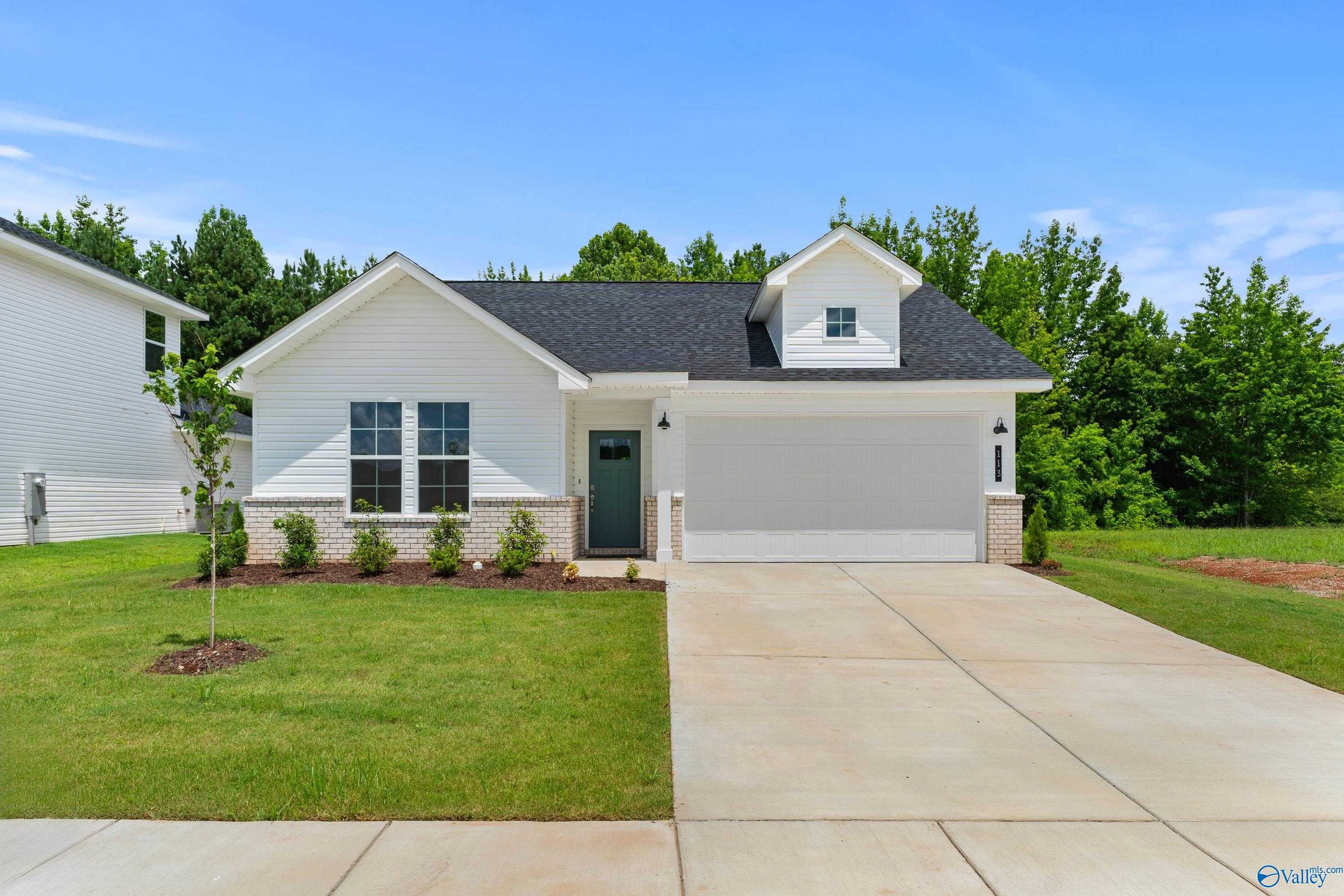 White single-story home with black roof, 2-car garage, landscaped yard and trees in Forest Glen, Hazel Green, Alabama