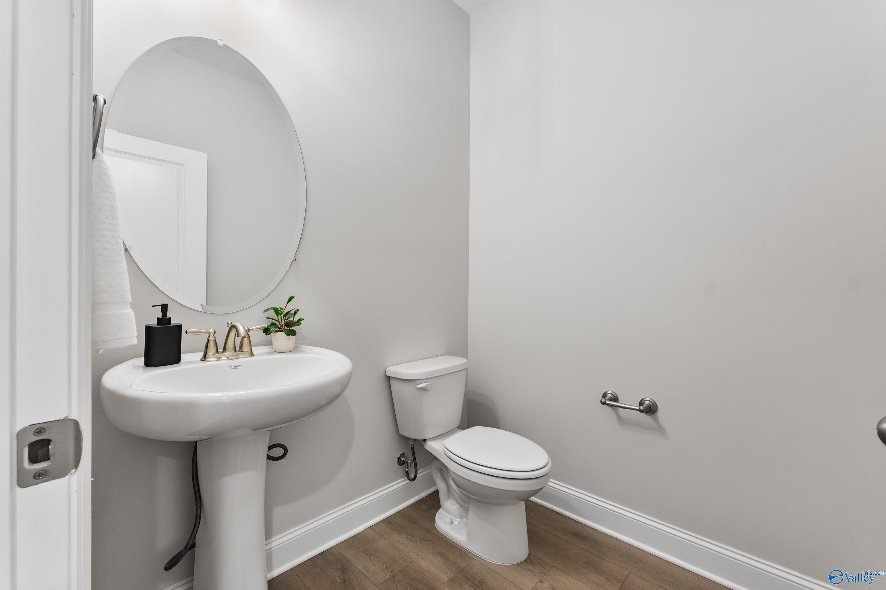 Elegant powder room with white pedestal sink, round mirror, and toilet in Davidson Homes The Finleigh, Toney, Alabama