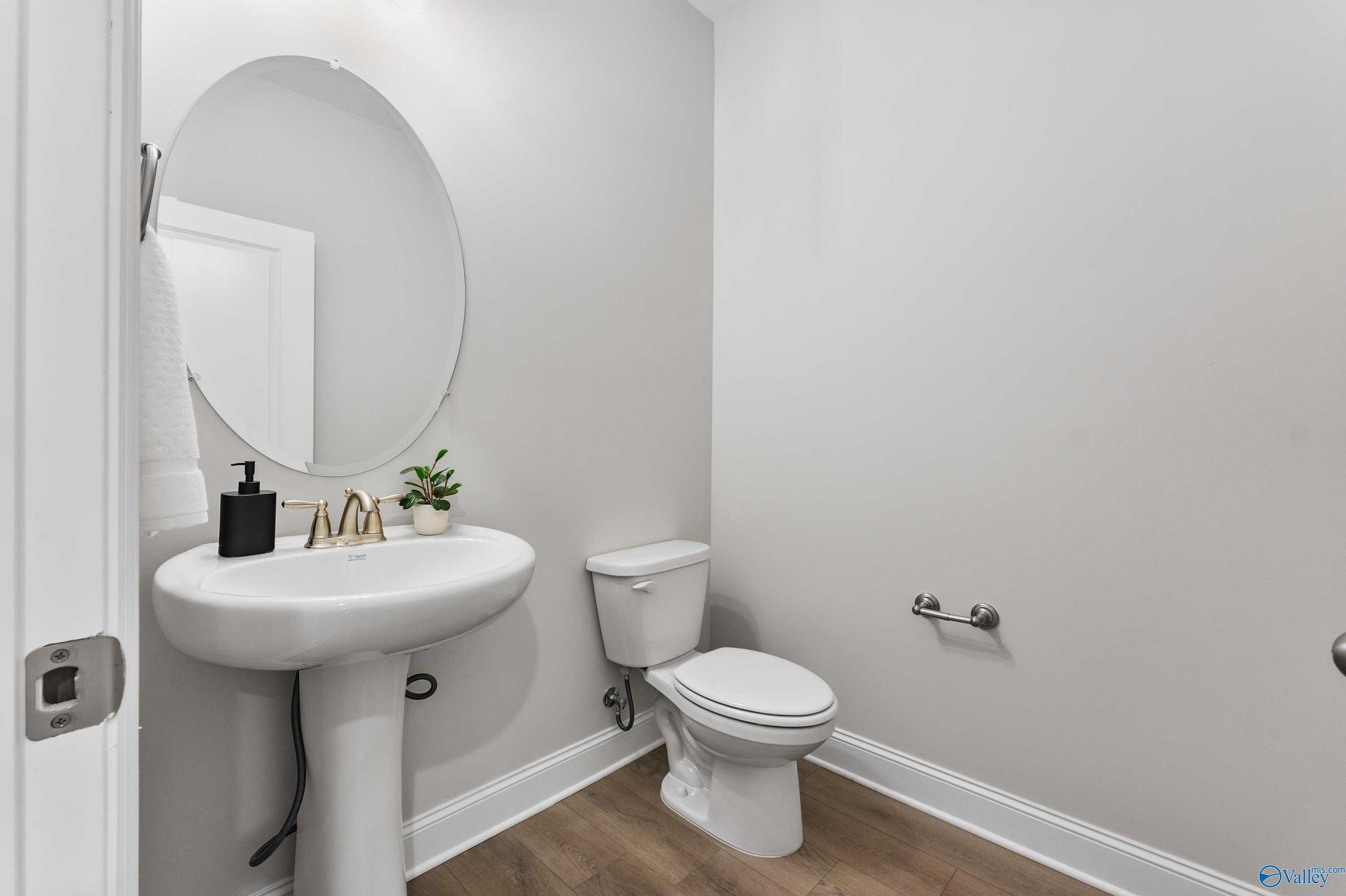 Elegant powder room with white pedestal sink, round mirror, and toilet in Davidson Homes The Finleigh, Toney, Alabama