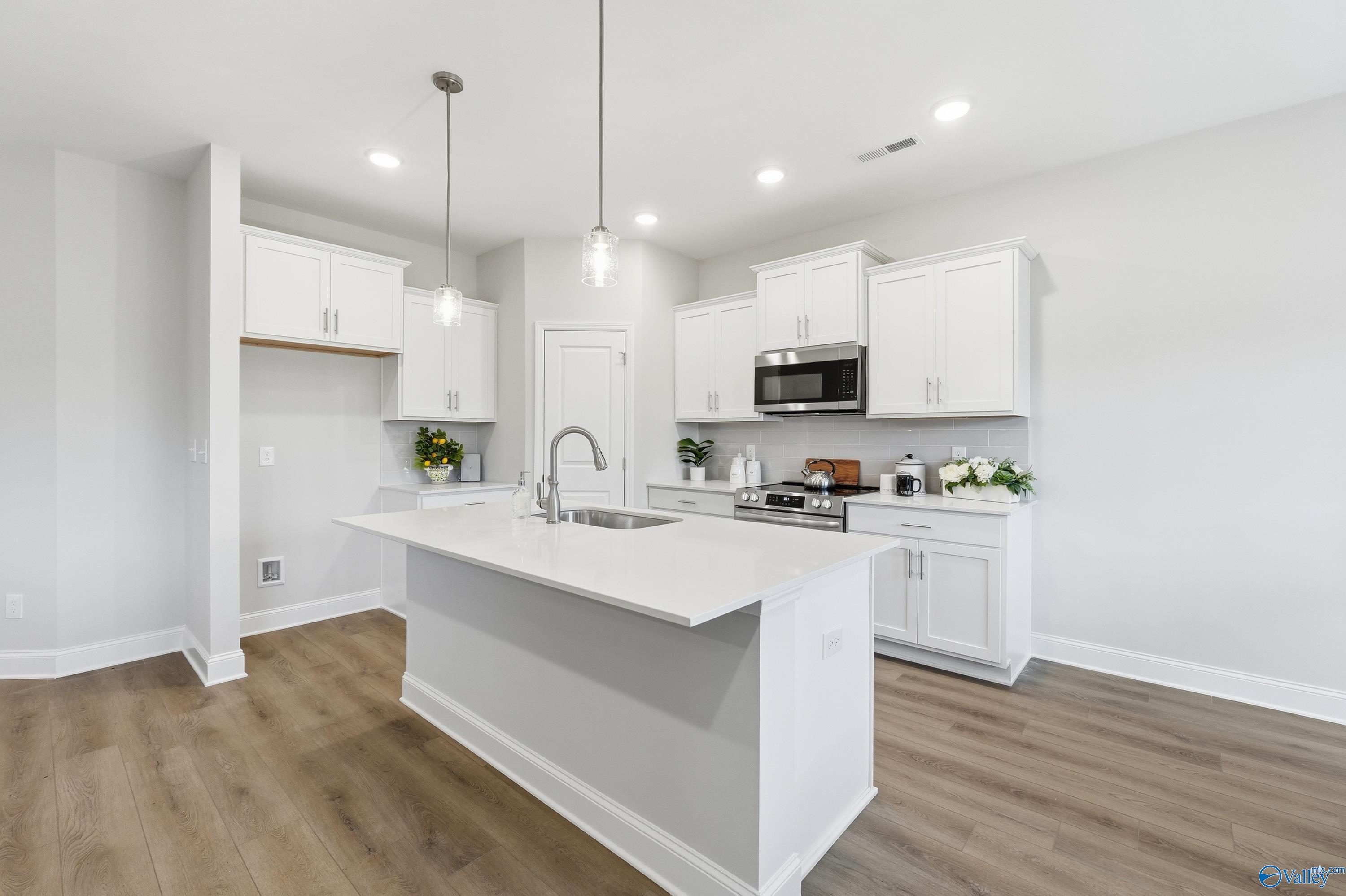 Modern white kitchen island with stainless steel appliances and pendant lights in Davidson Homes The Asheville, Toney, Alabama