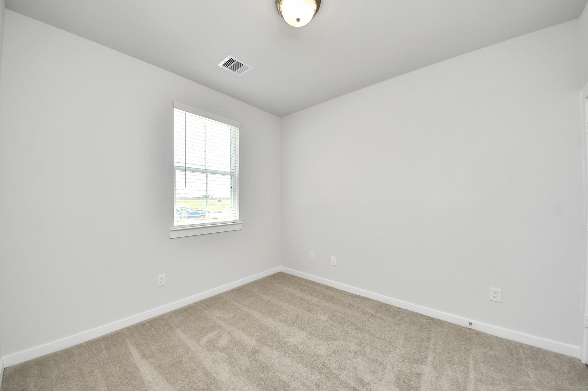 Bright empty bedroom with plush carpet, white walls, and window with blinds in Davidson Homes The Costa A plan in Beasley, Texas
