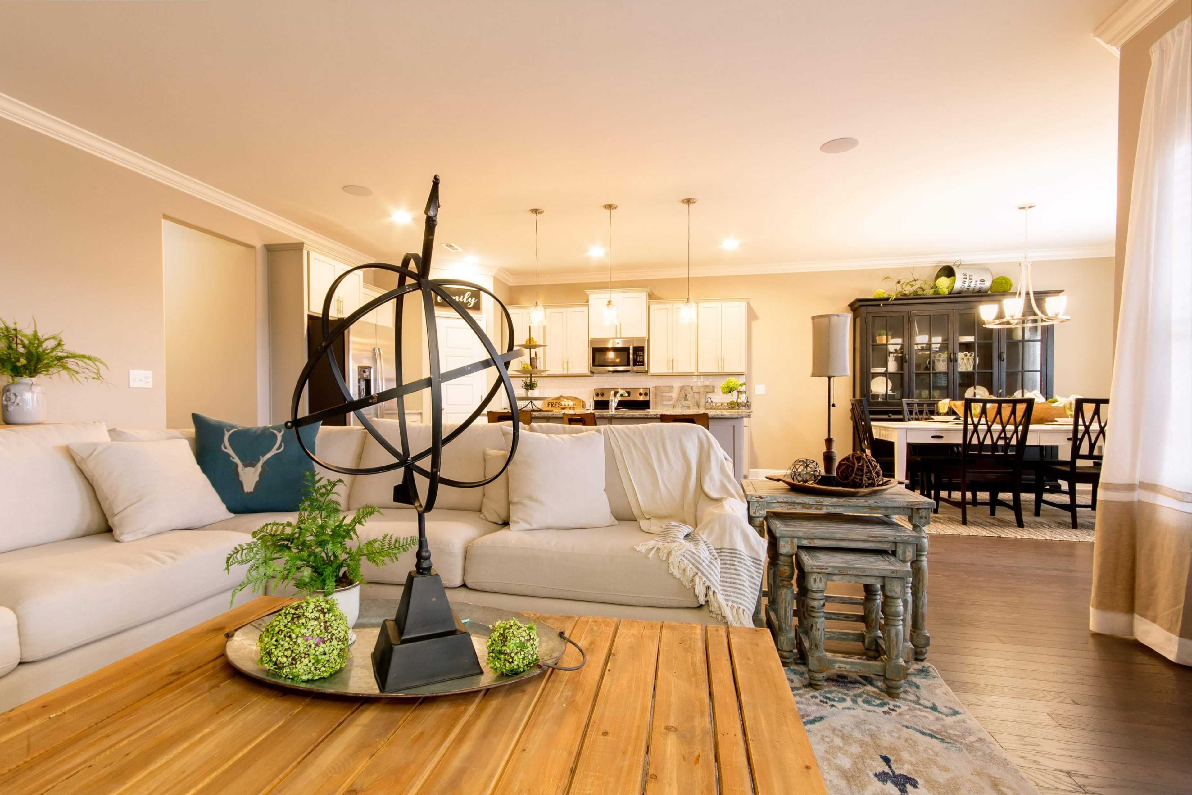 Open-concept living room in Bakers Farm home, Priceville AL by Davidson Homes featuring beige sofa, wooden coffee table, and adjacent kitchen with white cabinets