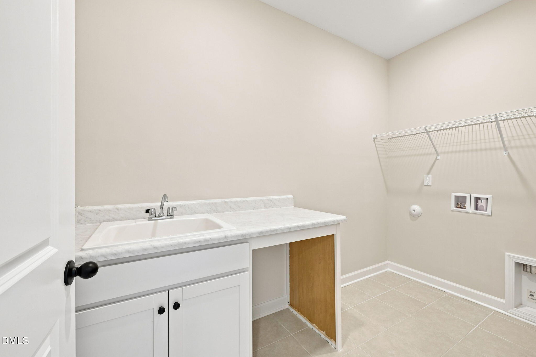 Laundry room with utility sink, white cabinetry, and wall shelving in The Harris C home at Forestville Yard, Knightdale, NC.