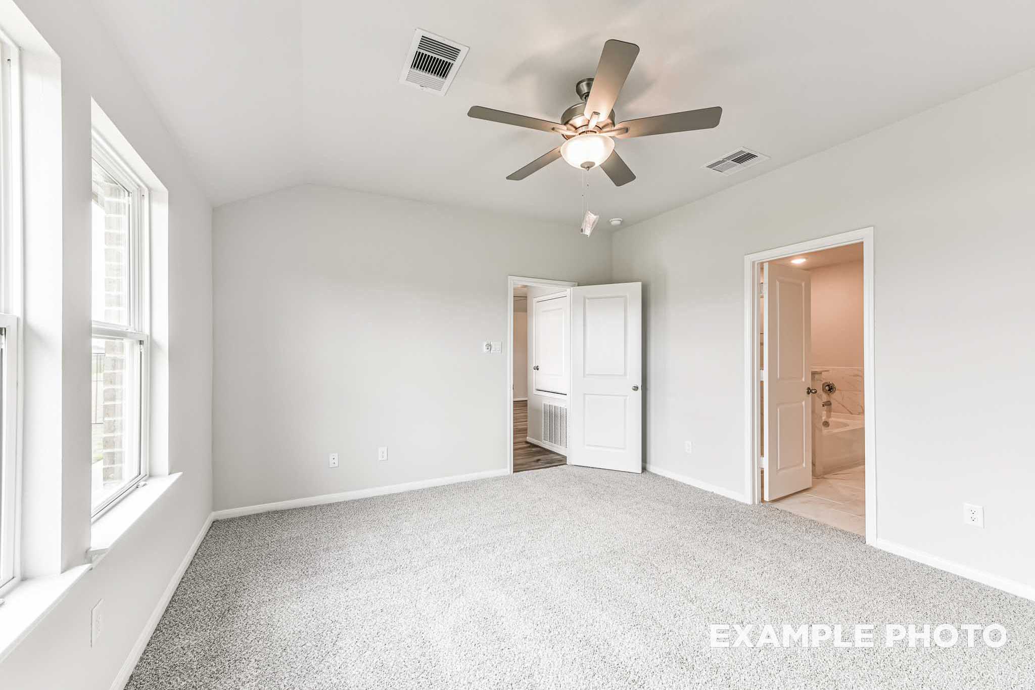 Spacious master bedroom in The Laguna B with gray carpet, ceiling fan, large windows, and ensuite bath access