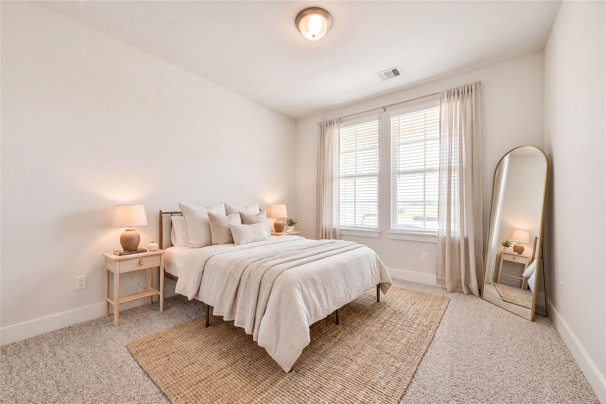Elegant bedroom with neutral king bed, seagrass rug, gold full-length mirror, and large windows in Davidson Homes Victoria A, Lago Mar Texas