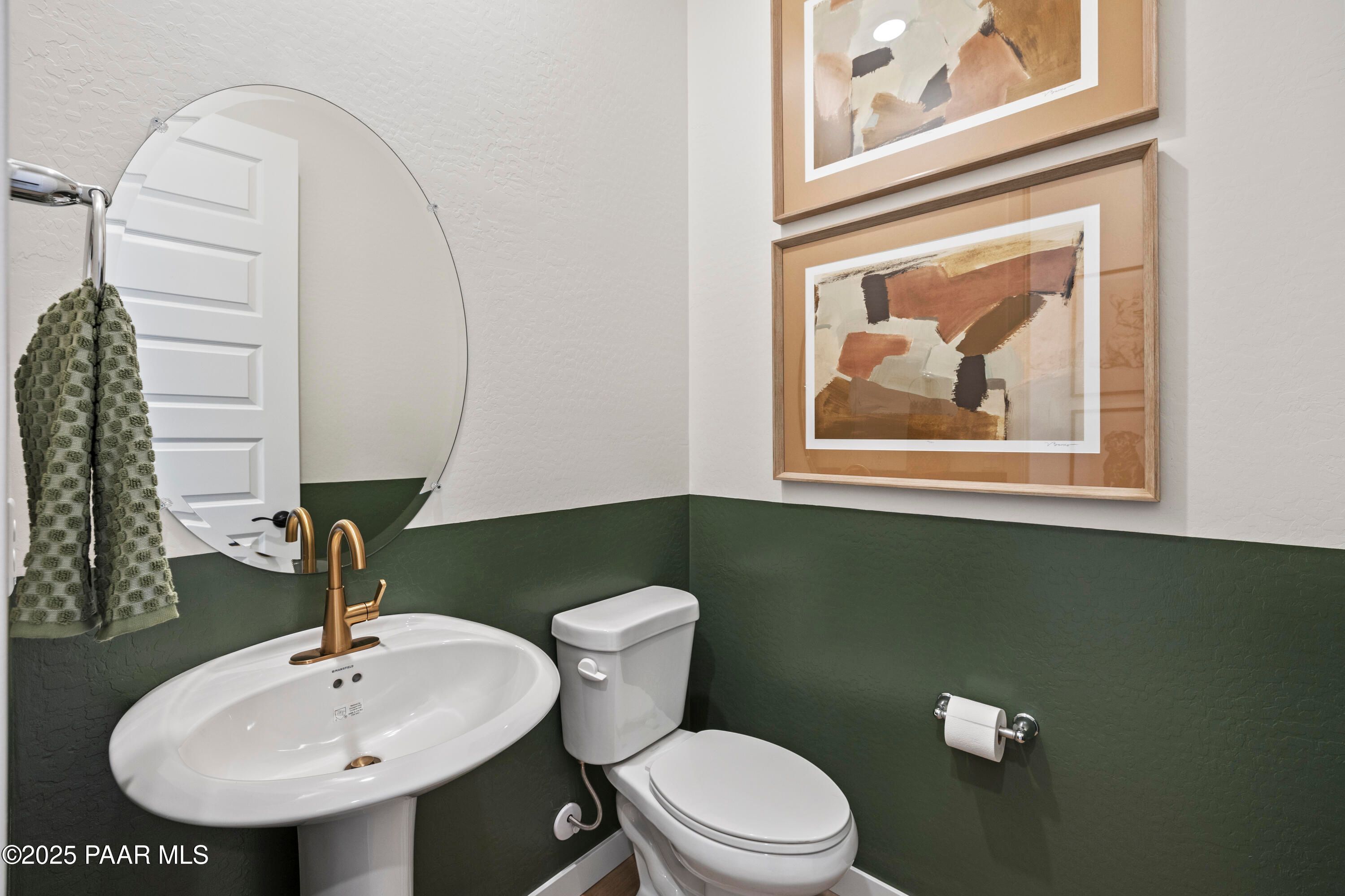 Modern powder room featuring round mirror, gold faucet sink, green accent wall, and abstract art in Davidson Homes The Blaze D, Prescott, Arizona