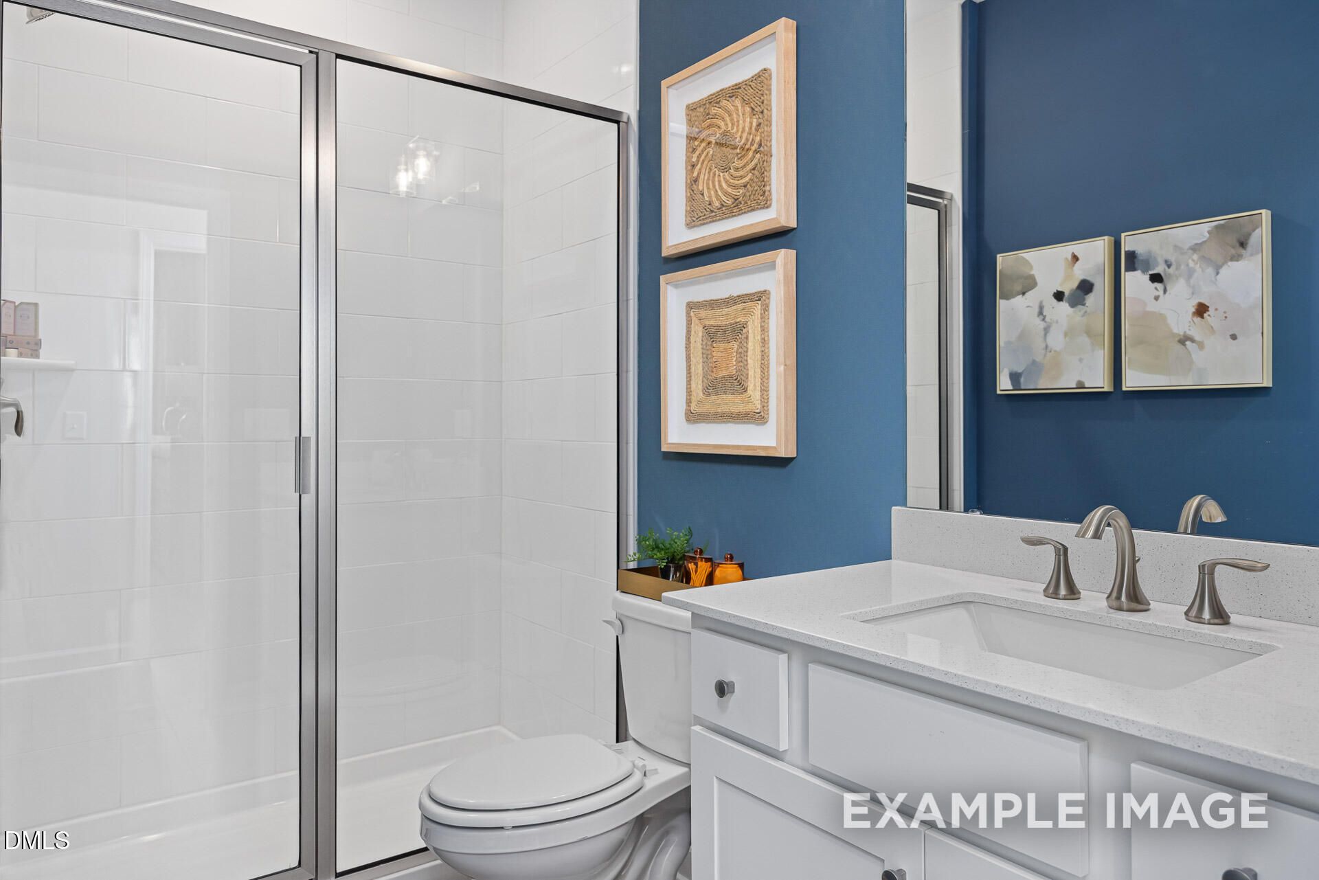 Modern bathroom with glass-enclosed shower, white vanity, and blue accent wall in The Adalynn A home, Woodland Crossing.