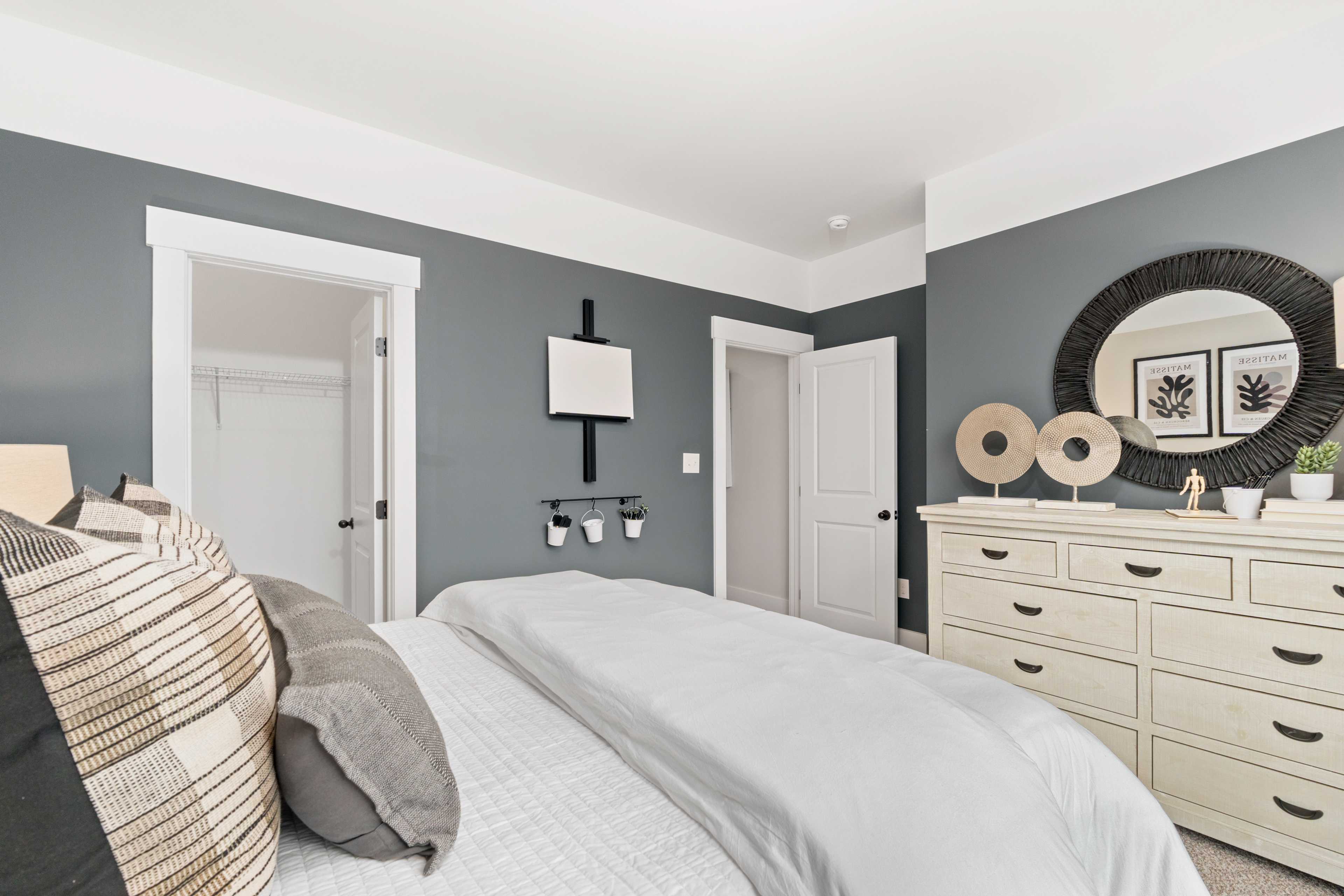 Spacious bedroom at Kendall Farms in Toney, Alabama with gray walls, white bed, dresser, and round mirror