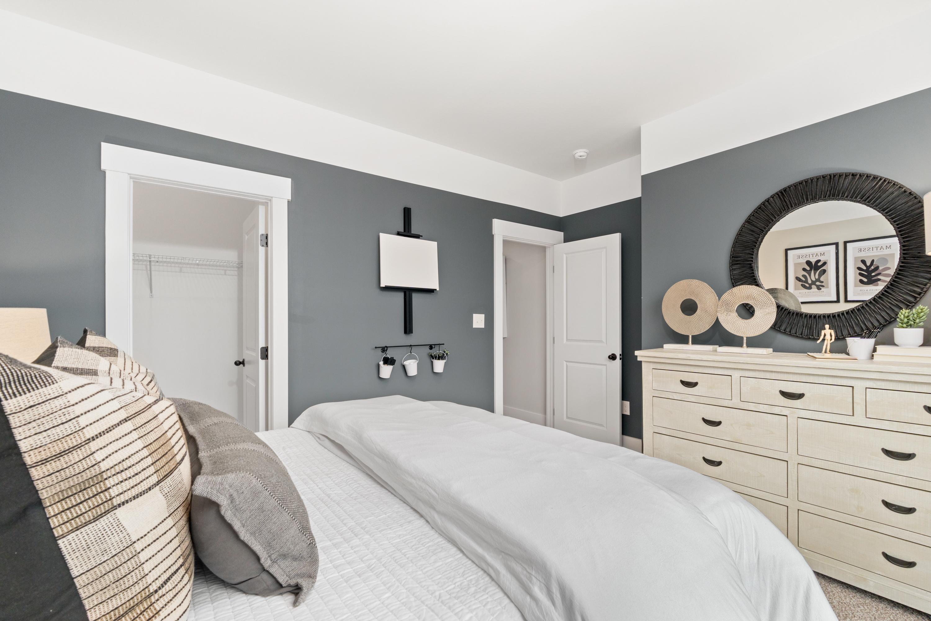 Spacious bedroom at Kendall Farms in Toney, Alabama with gray walls, white bed, dresser, and round mirror