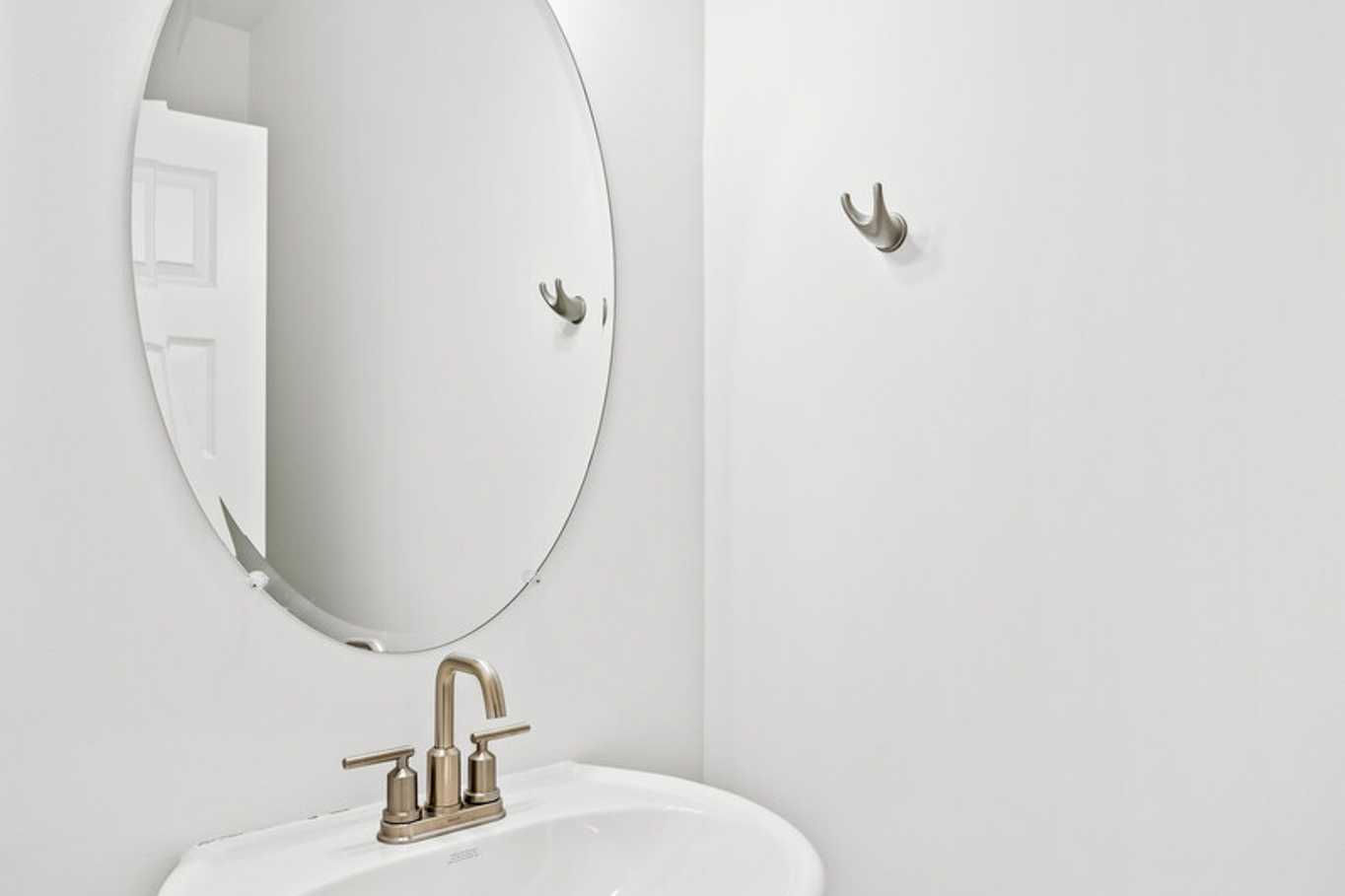 Modern powder room in The Murray B with white pedestal sink, oval mirror, and globe light fixture by Davidson Homes