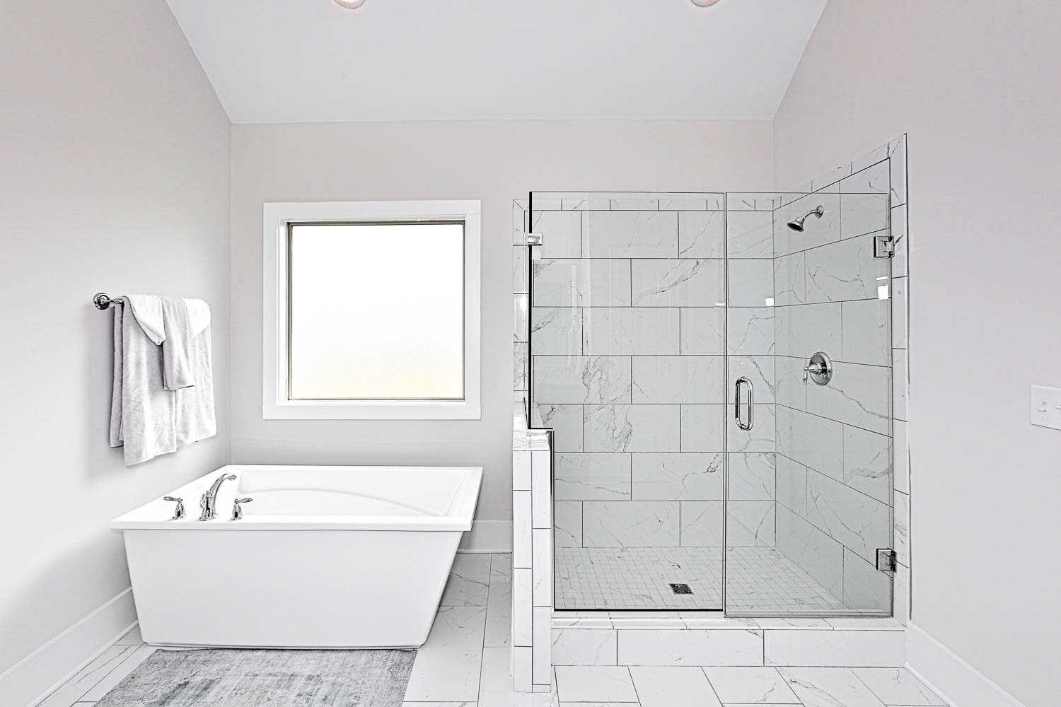 Spacious master bathroom in The Finleigh with freestanding white tub, frameless glass shower, subway tile, and large window
