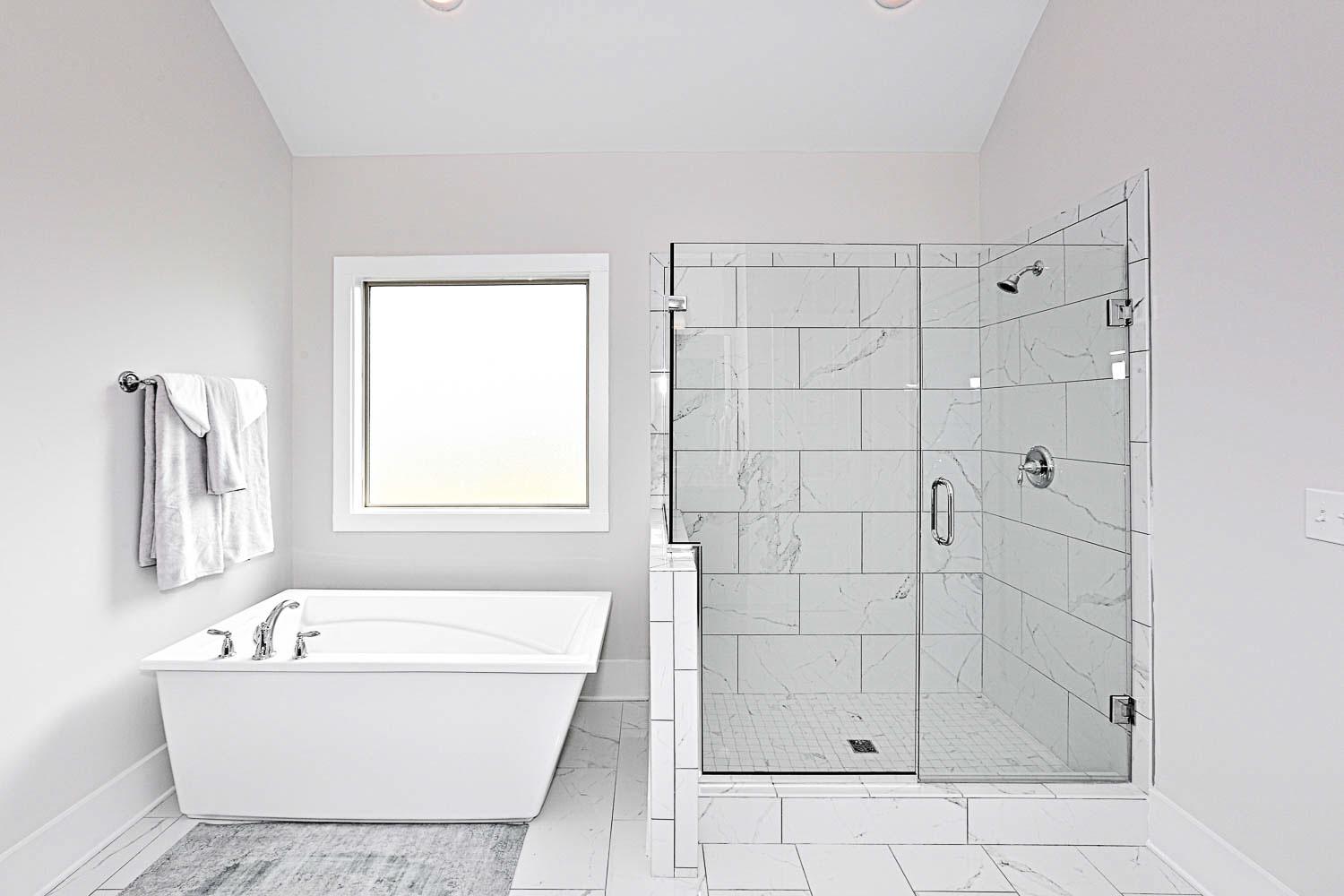 Spacious master bathroom in The Finleigh featuring freestanding tub, frameless glass shower, and marble tiles