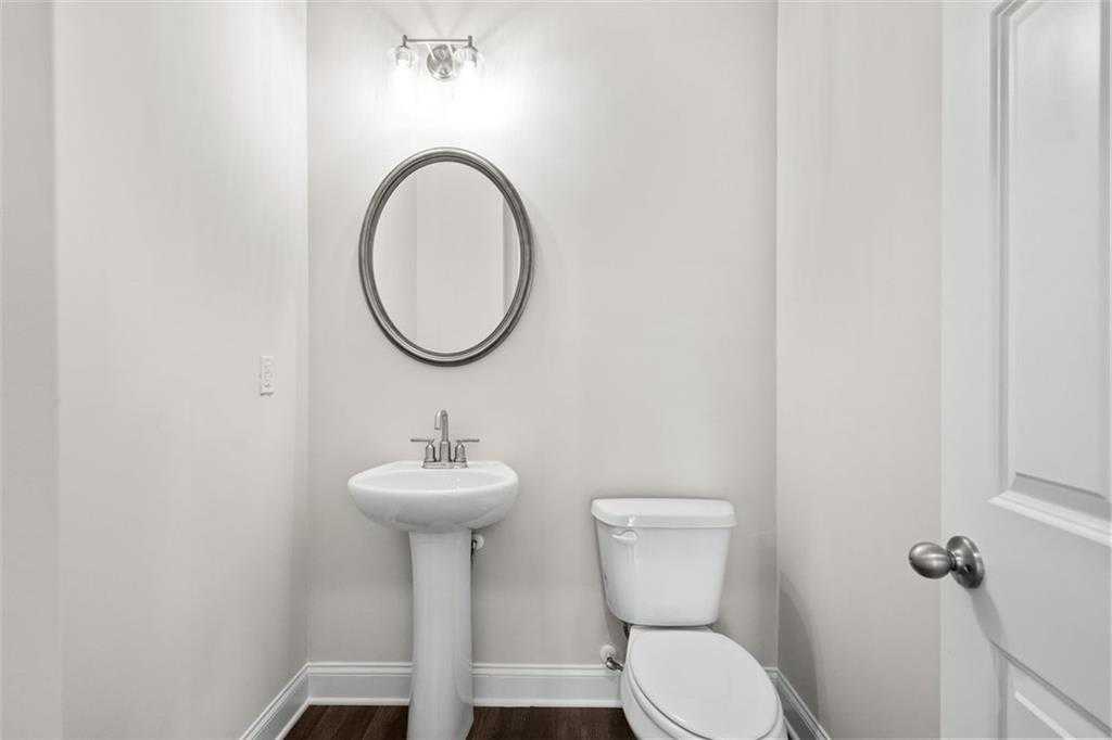 Elegant powder room featuring pedestal sink, round mirror, and toilet in Davidson Homes The Ash C at Wehunt Meadows, Hoschton, Georgia