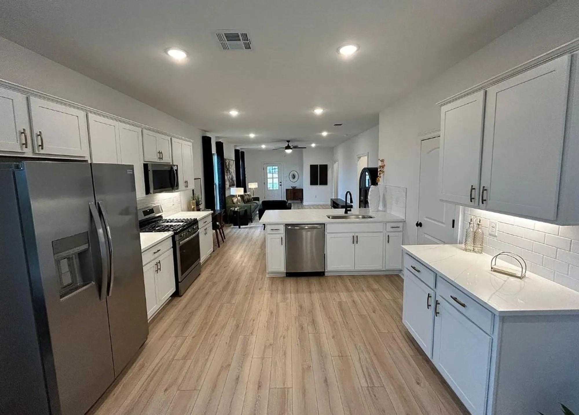 Modern open-concept kitchen featuring white shaker cabinets, stainless steel appliances, quartz island, and subway tile backsplash in Davidson Homes The Luna J, Katy, Texas